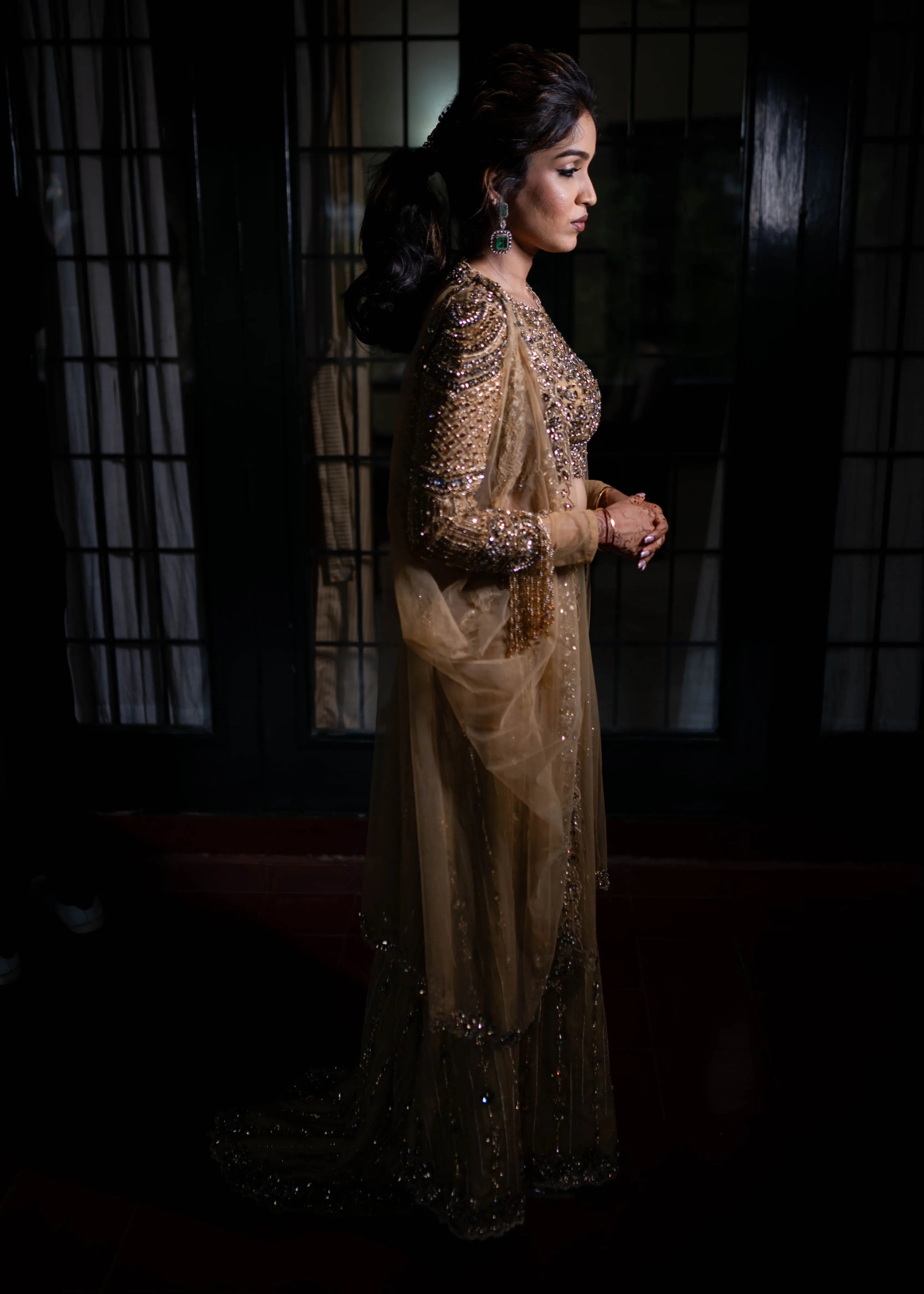 Bride posing for side profile in a concept gold lehenga in tulle designed by Archana Karthick is handcrafted intricately with rhinestones, crystal beads, cutdanas and sequins.