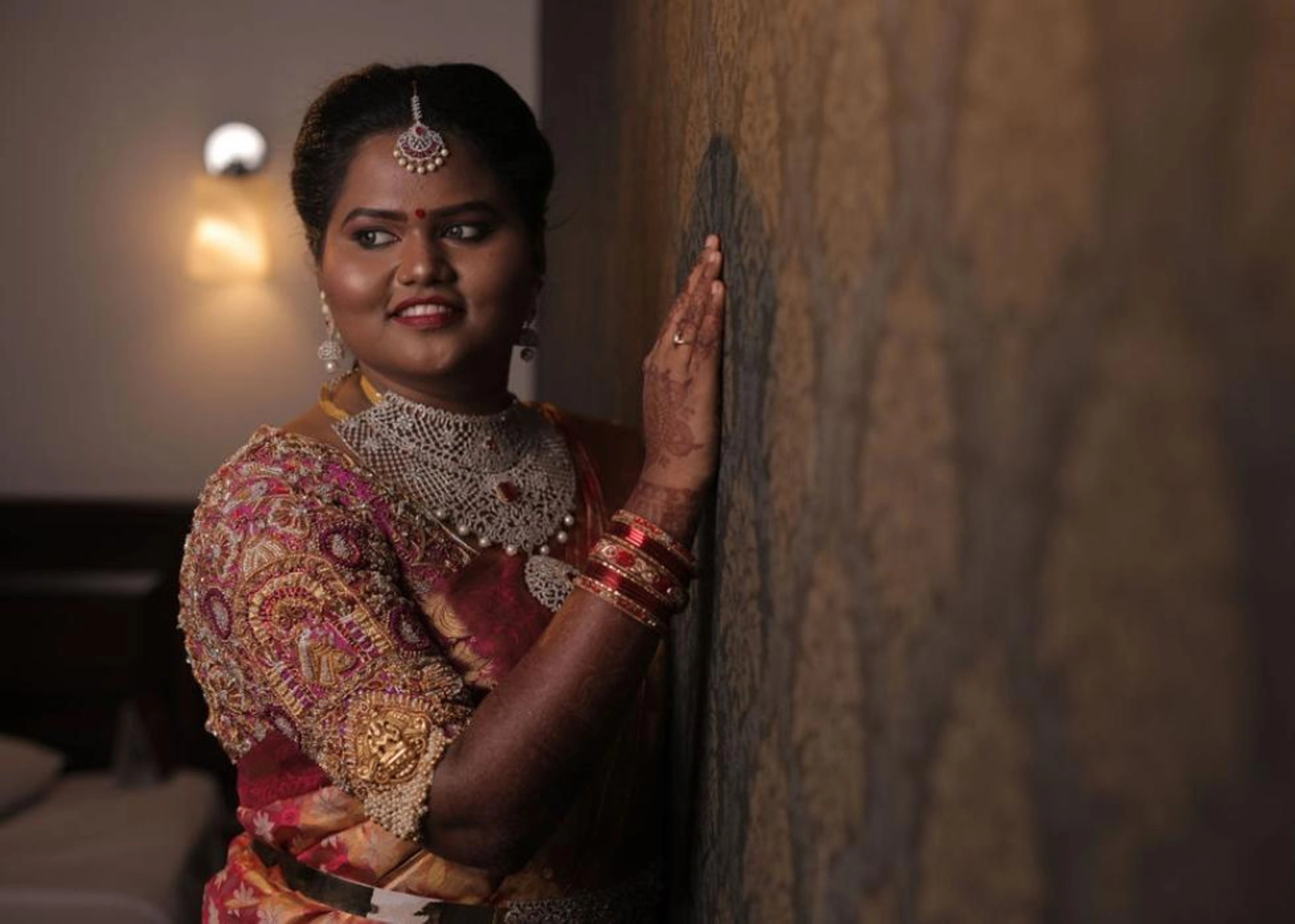 Bride posing in a handcrafted palanquin concept magenta pink silk blouse with zardozi, kemp stones, pearls and resham knot work and goddess pendants on each sleeve. Designed by Archana Karthick