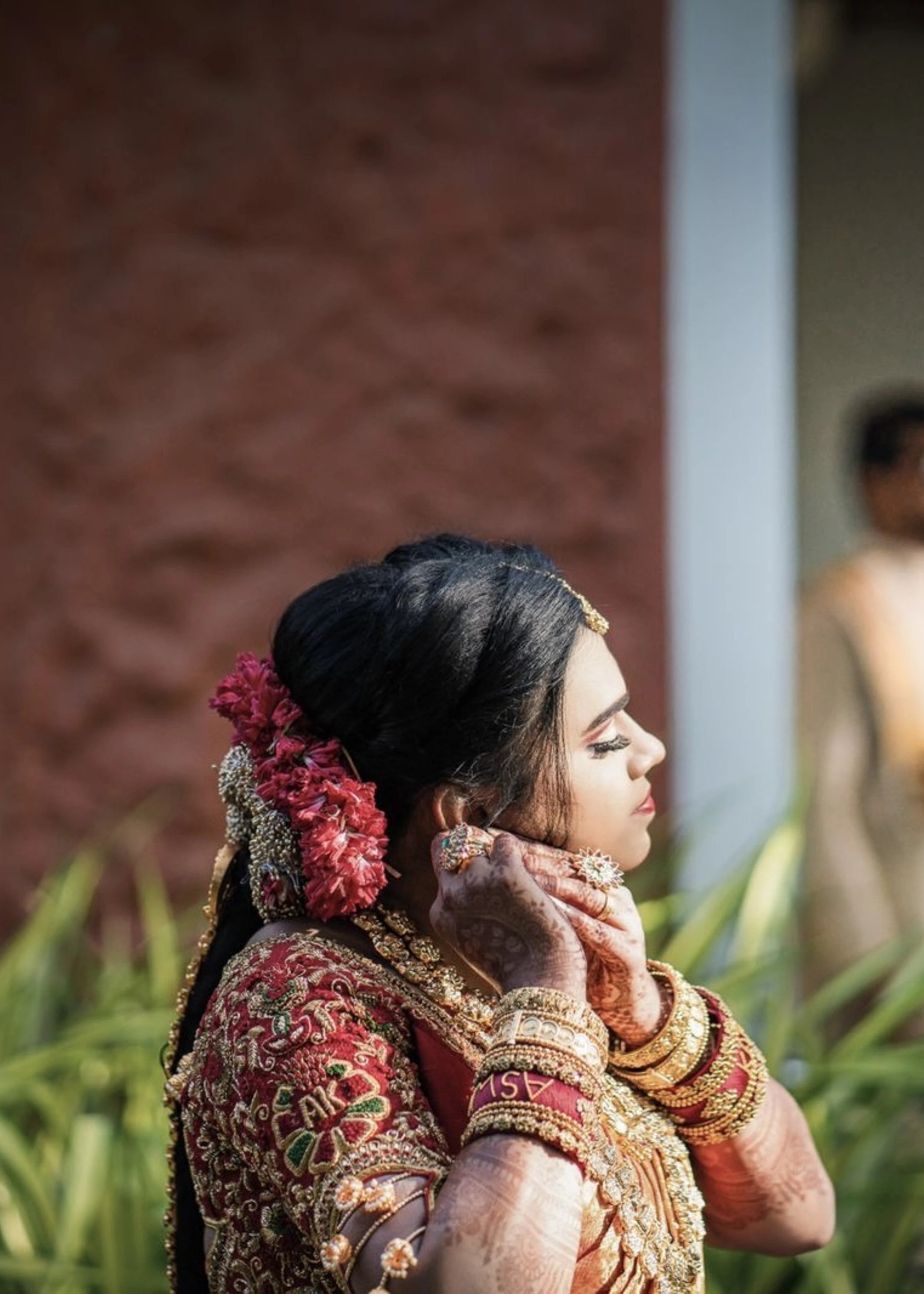 Bride posing in a red raw silk blouse handcrafted with beads, stones, zardozi, resham knot work and jhumki hangings with creeper motifs designed by Archana Karthick