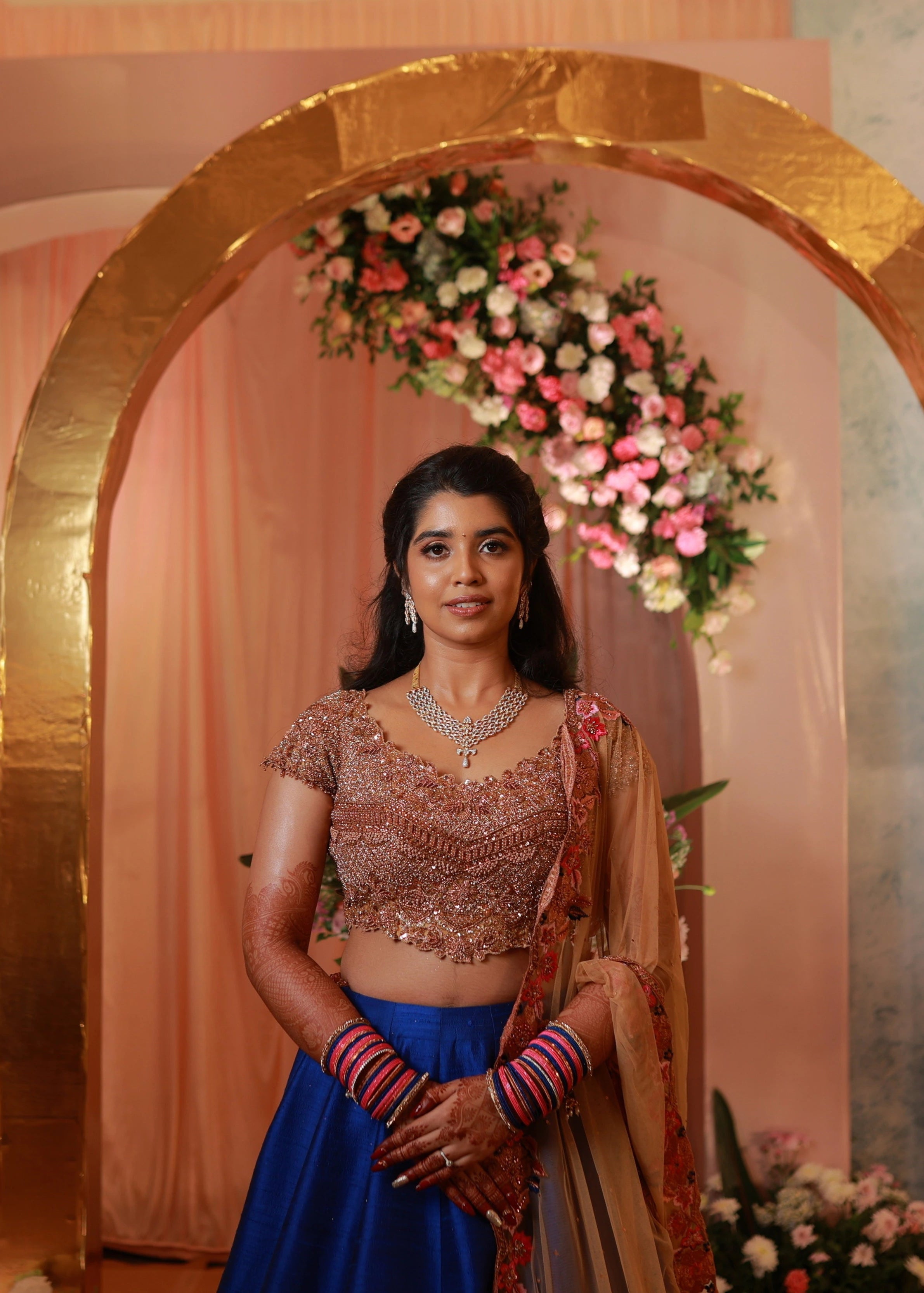 Bride posing in rose gold and blue lehenga handcrafted with stone work, cut dana, sequins, resham and cut worked dupatta border designed by Archana Karthick