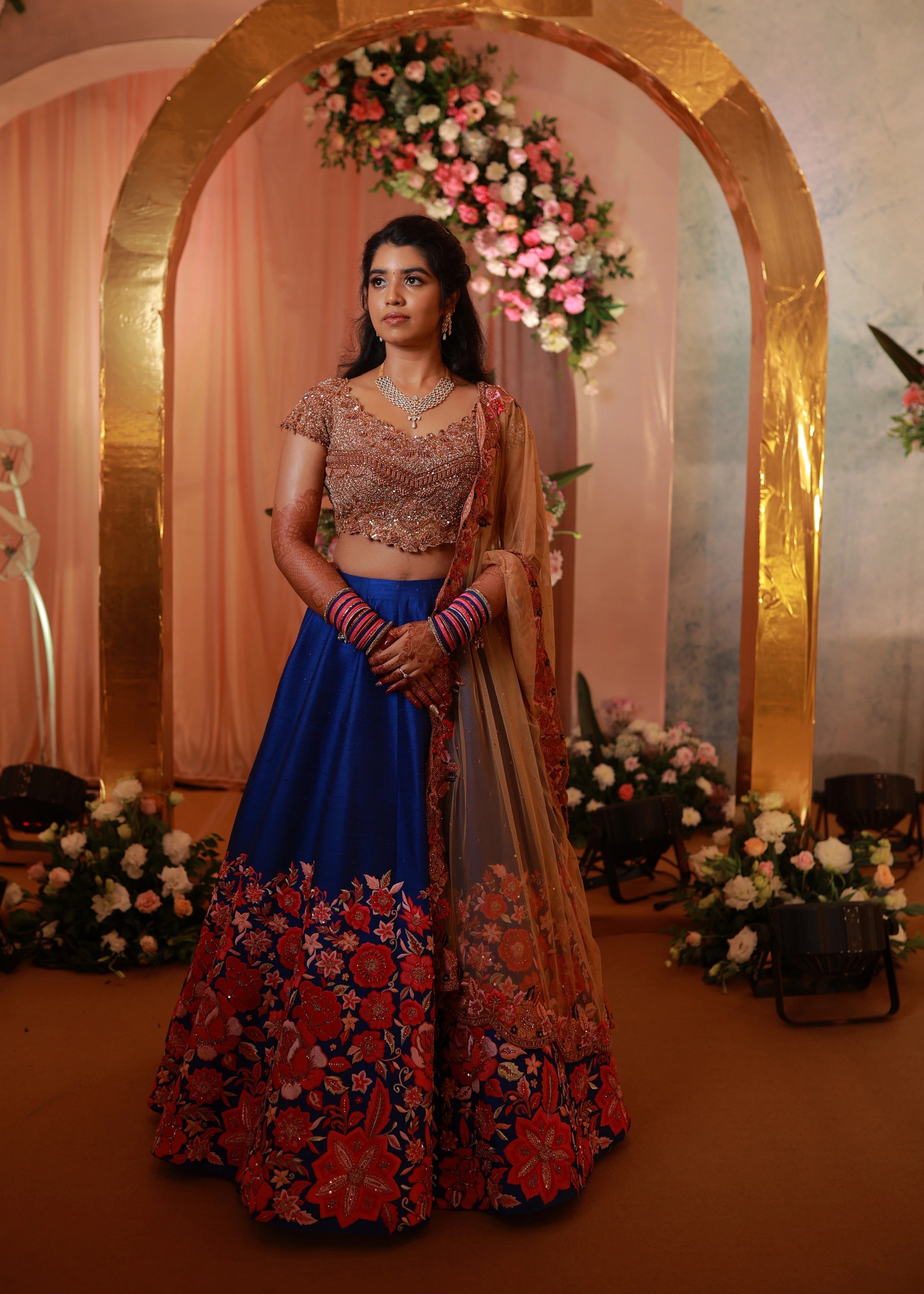 Bride posing on stage in rose gold and blue lehenga handcrafted with stone work, cut dana, sequins, resham and cut worked dupatta border designed by Archana Karthick