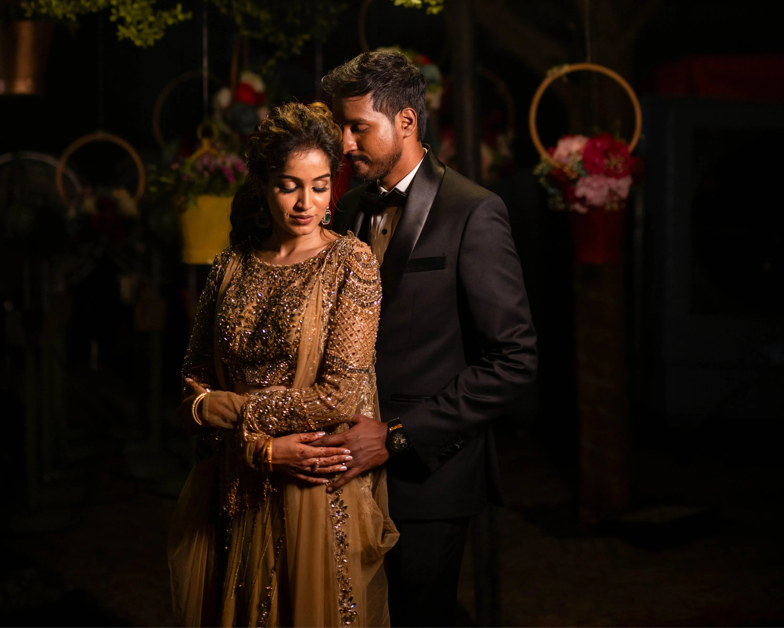Bride posing with groom in a concept gold lehenga in tulle designed by Archana Karthick is handcrafted intricately with rhinestones, crystal beads, cutdanas and sequins.