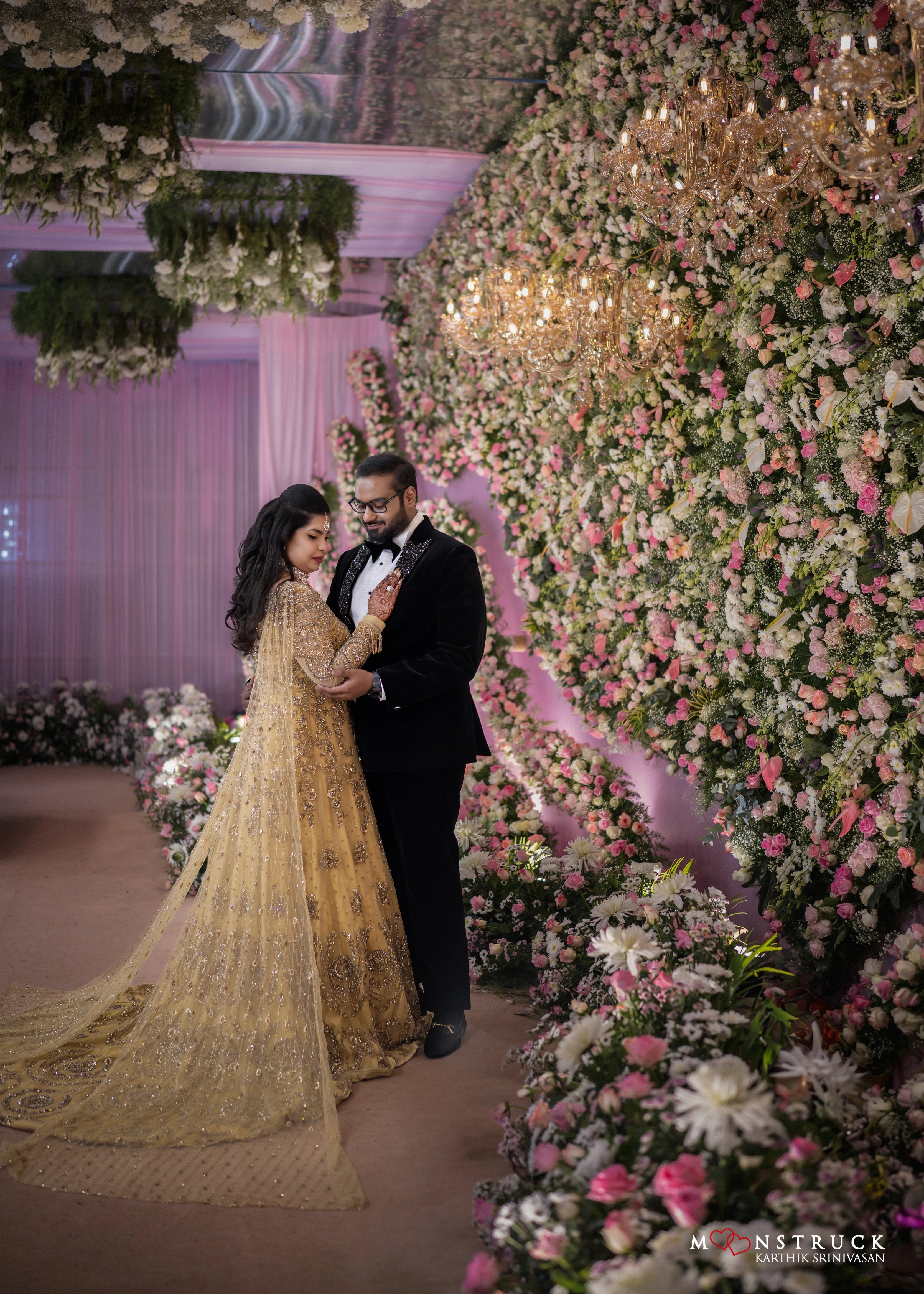 Bride posing with groom in a gold gown in tulle designed by Archana Karthick and handcrafted with rhinestones and cut dana with floral and geometric motifs.