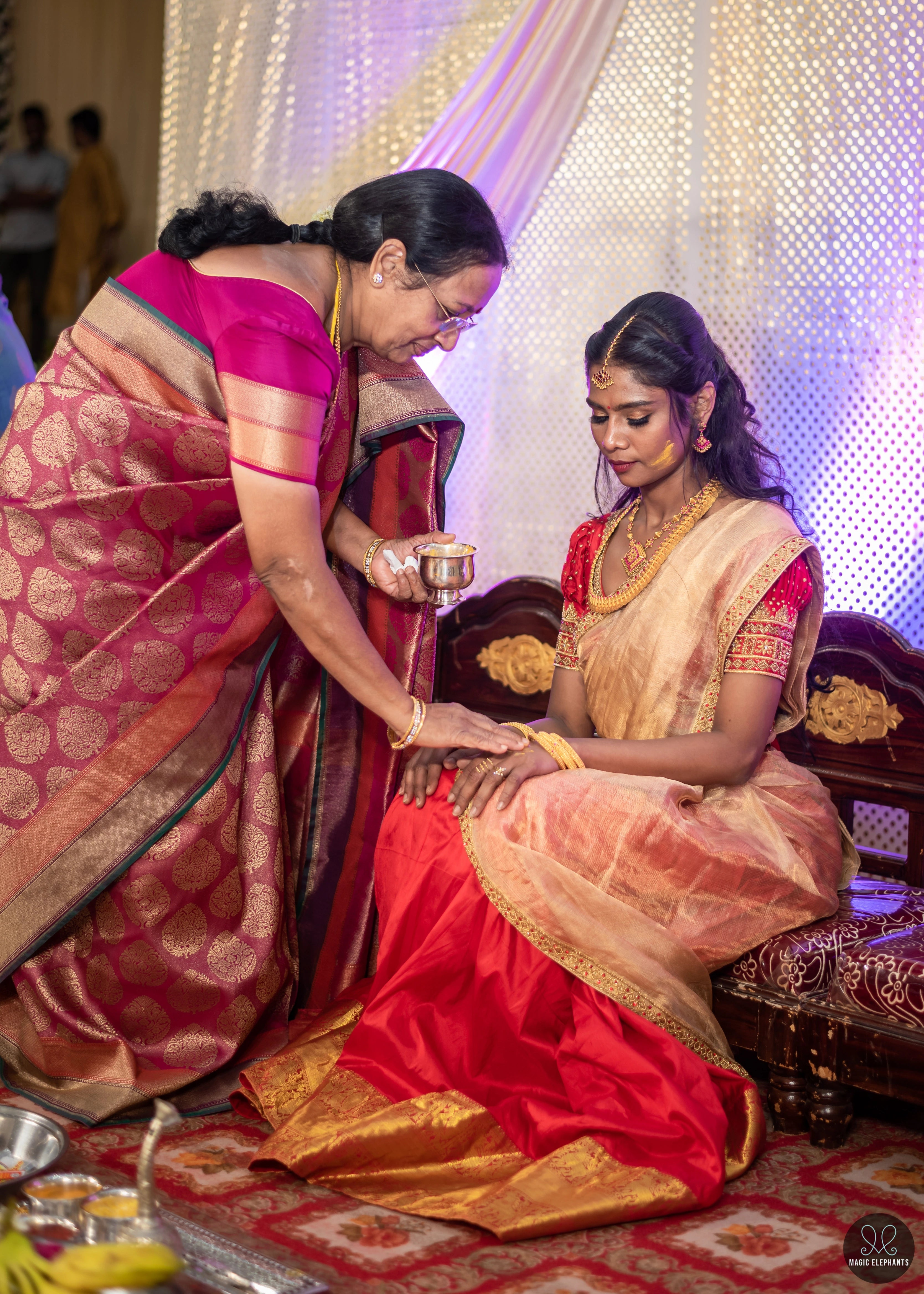 Bride receiving blessings in a handcrafted red silk half saree with katori cut blouse has intricate zardozi and stone work.