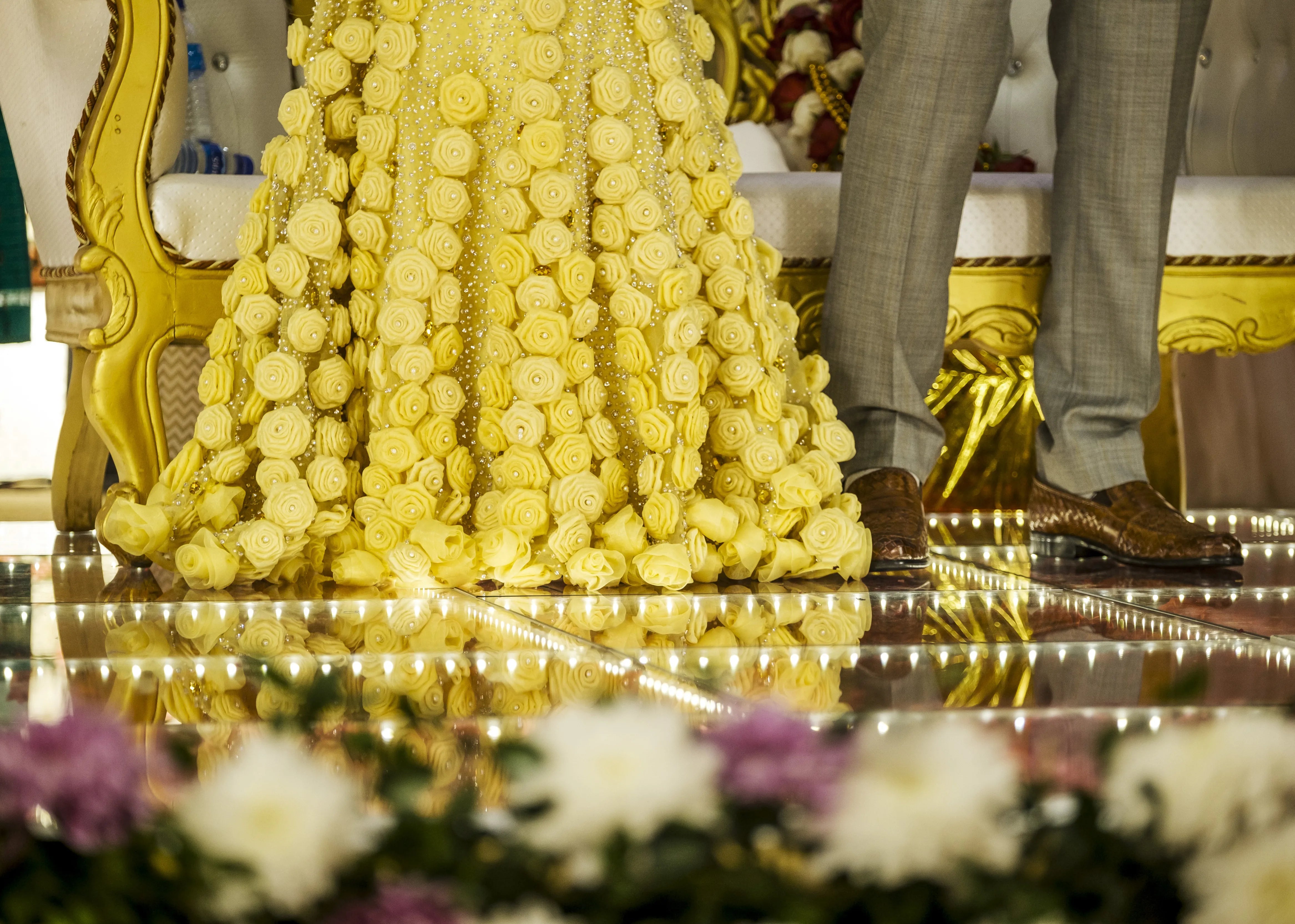 Bride's outfit highlighted on stage with groom in handcrafted yellow mermaid lehenga embellished with cut dana, pearls, rhinestones and handmade 3D flowers.