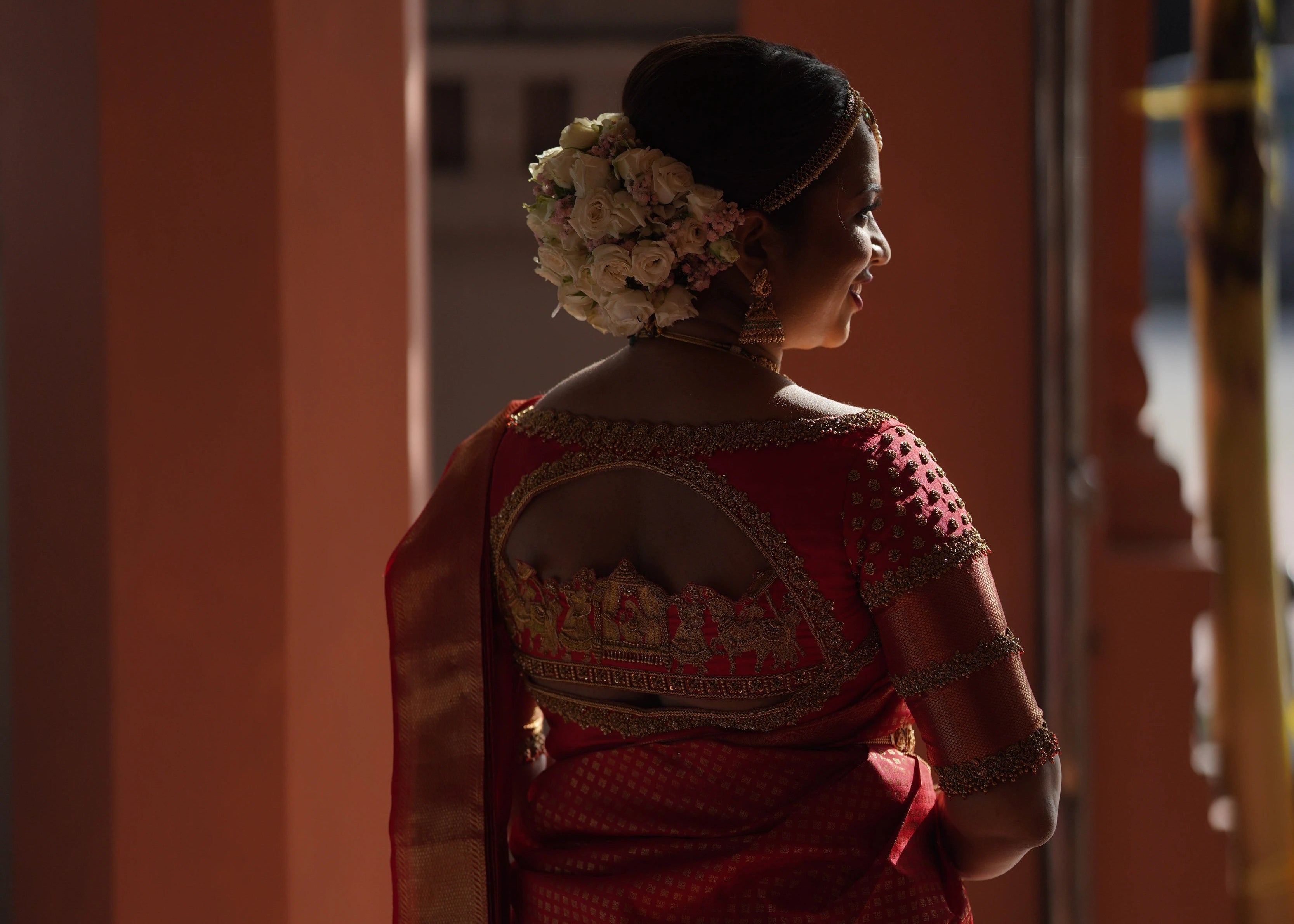 Bride showcasing back blouse design in a handcrafted palanquin concept red silk blouse features zardozi and beads. Designed by Archana Karthick.