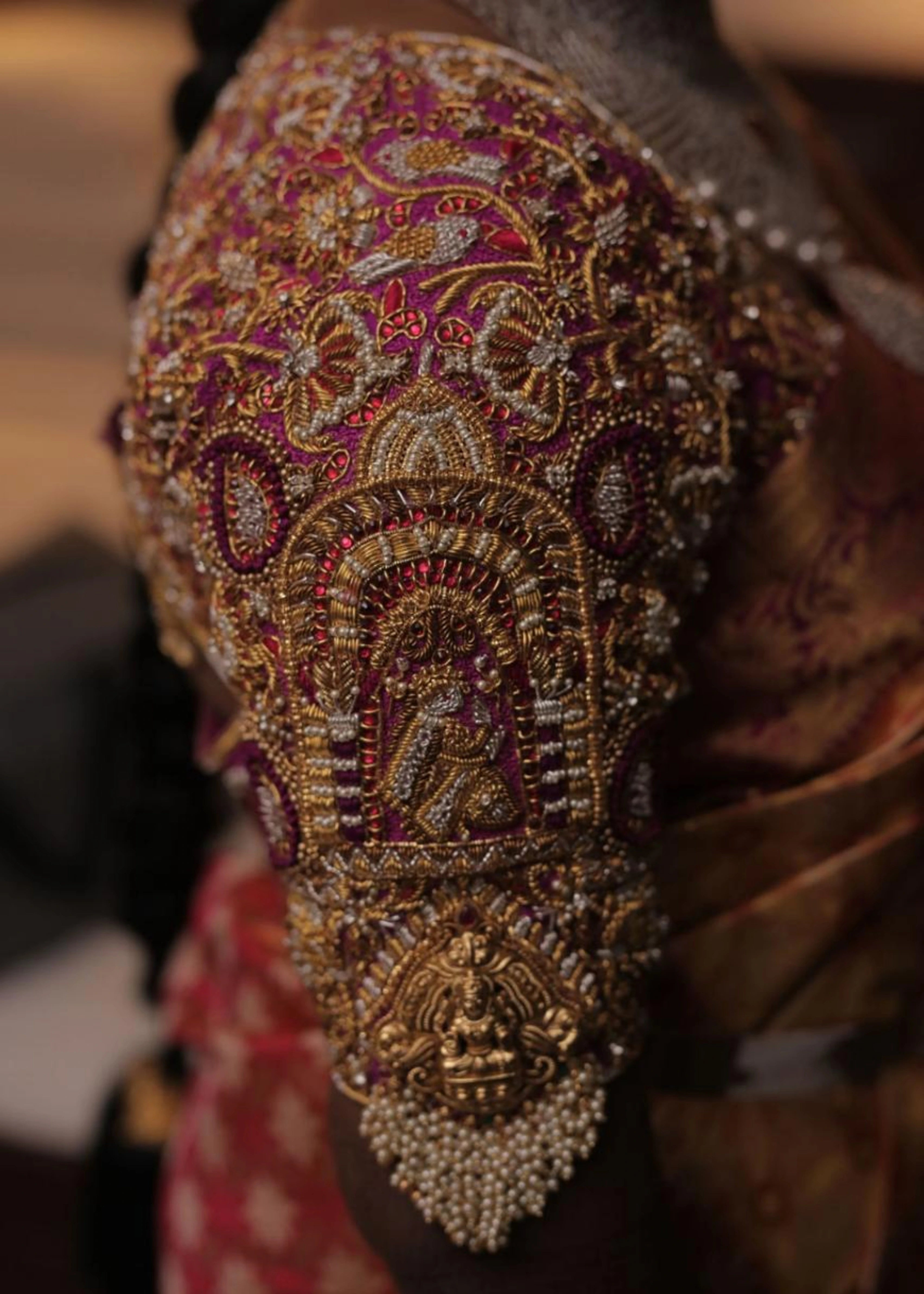 Bride showcasing the sleeve in a handcrafted palanquin concept magenta pink silk blouse with zardozi, kemp stones, pearls and resham knot work and goddess pendants on each sleeve. Designed by Archana Karthick