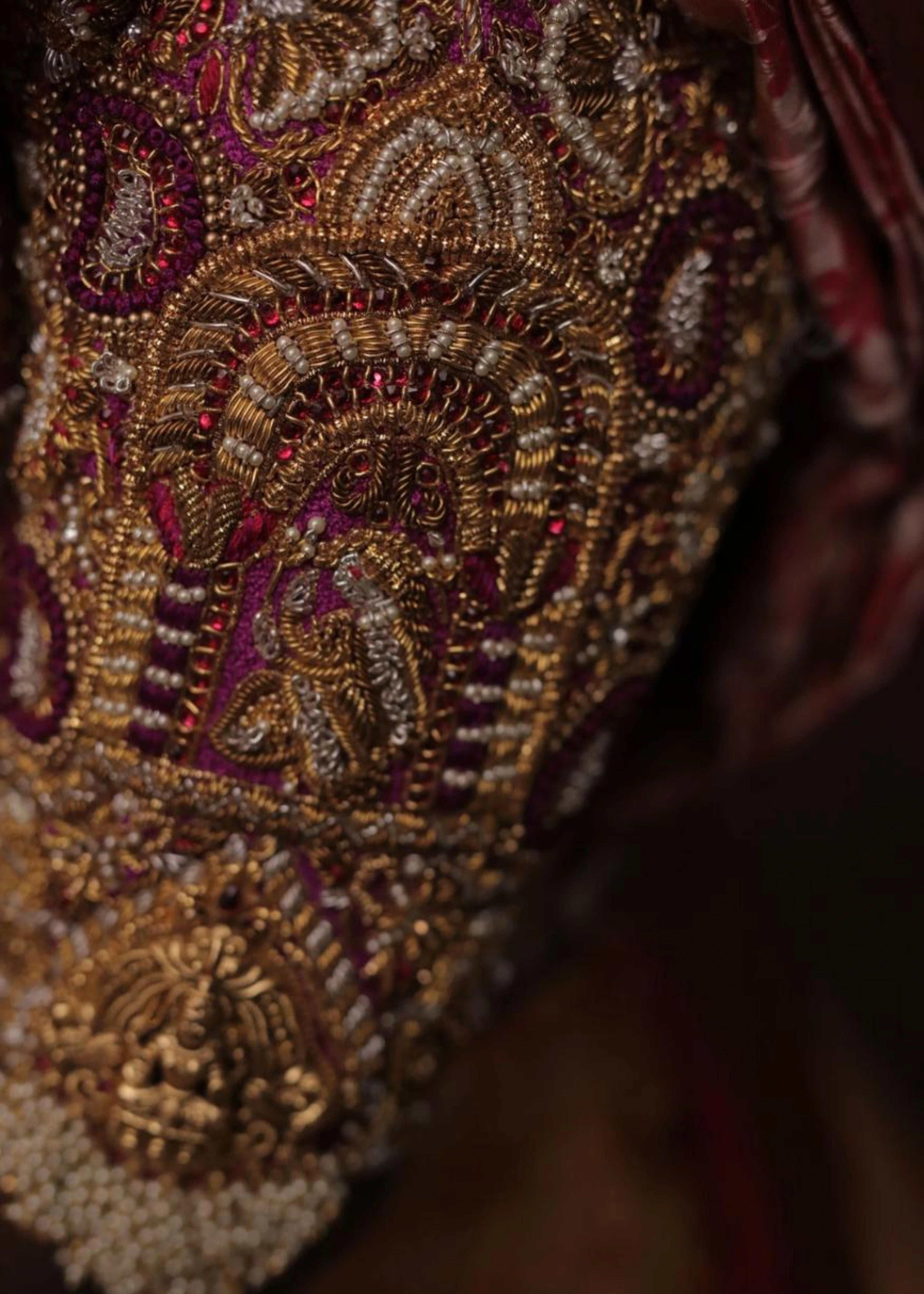 Bride showing the sleeve detailing in a handcrafted palanquin concept magenta pink silk blouse with zardozi, kemp stones, pearls and resham knot work and goddess pendants on each sleeve. Designed by Archana Karthick