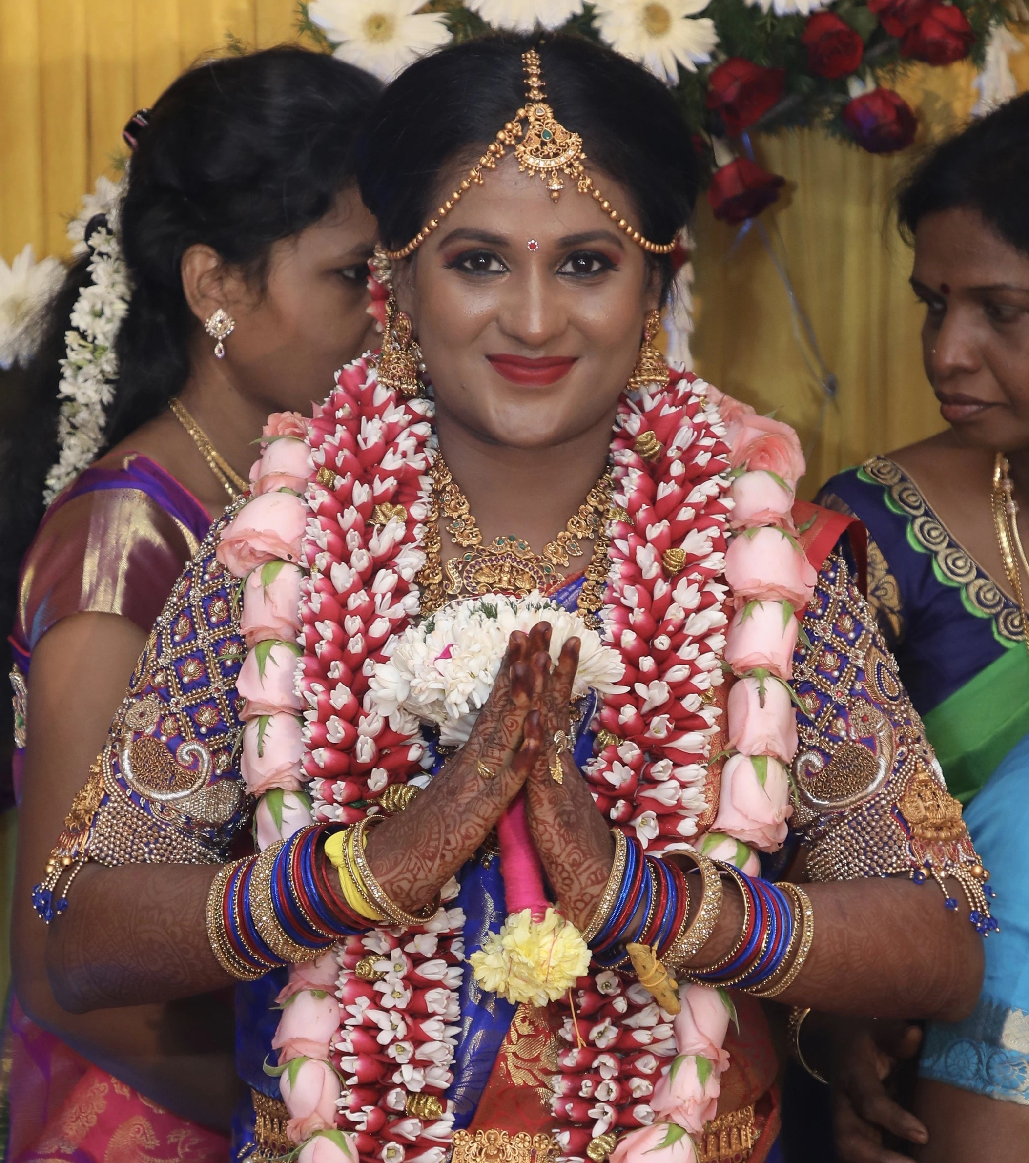Bride smiling at camera in a concept peacock blouse in blue and red silk, handcrafted with zardozi, beads, resham knot work and goddess pendant on sleeves.