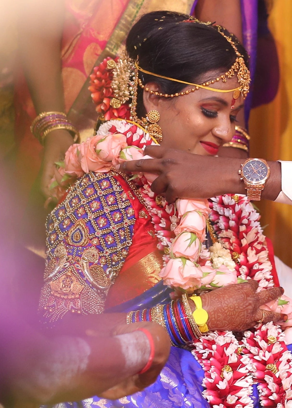 Bride smiling in a concept peacock blouse in blue and red silk, handcrafted with zardozi, beads, resham knot work and goddess pendant on sleeves.