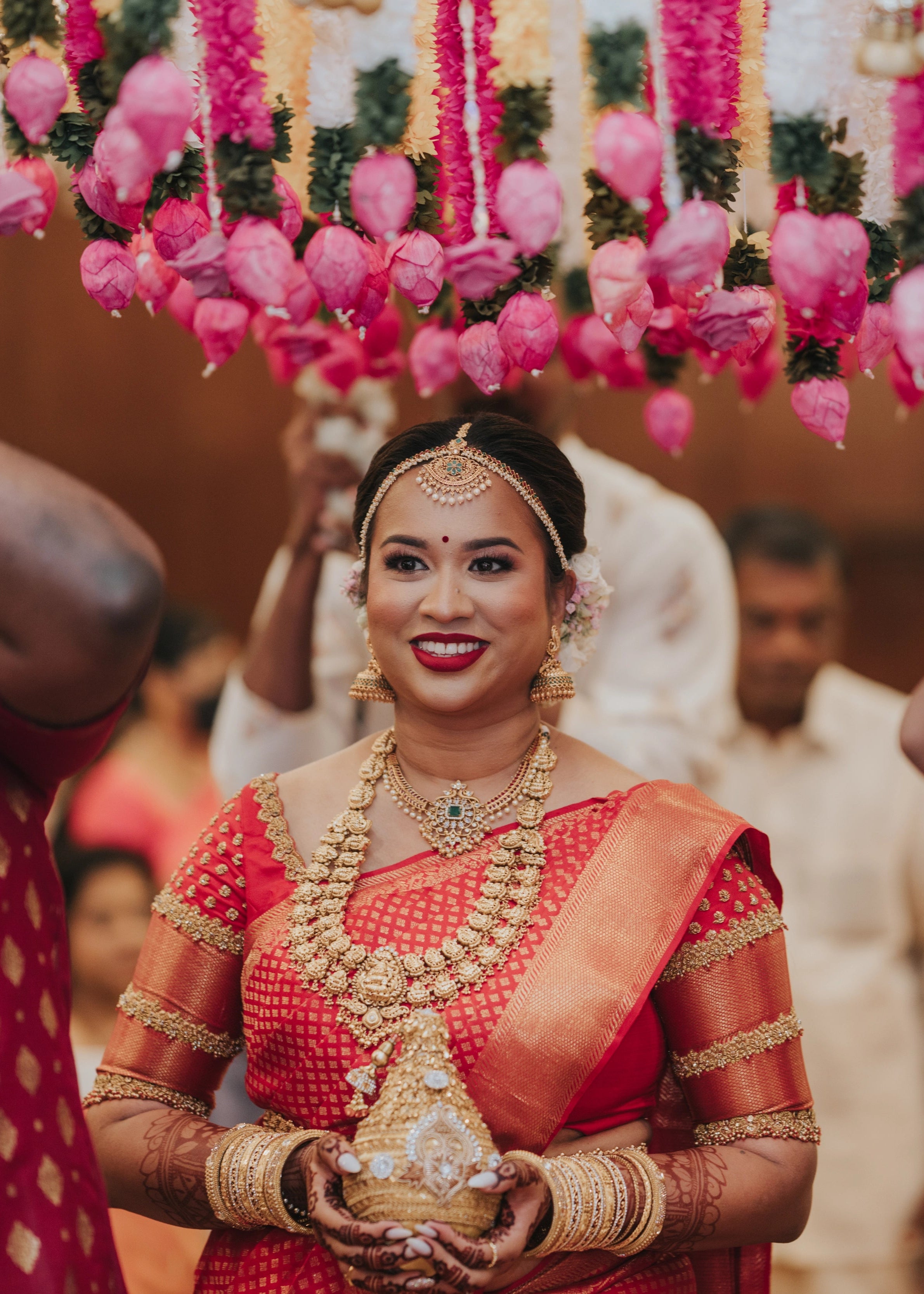 Bride smiling in a handcrafted palanquin concept red silk blouse features zardozi and beads. Designed by Archana Karthick.