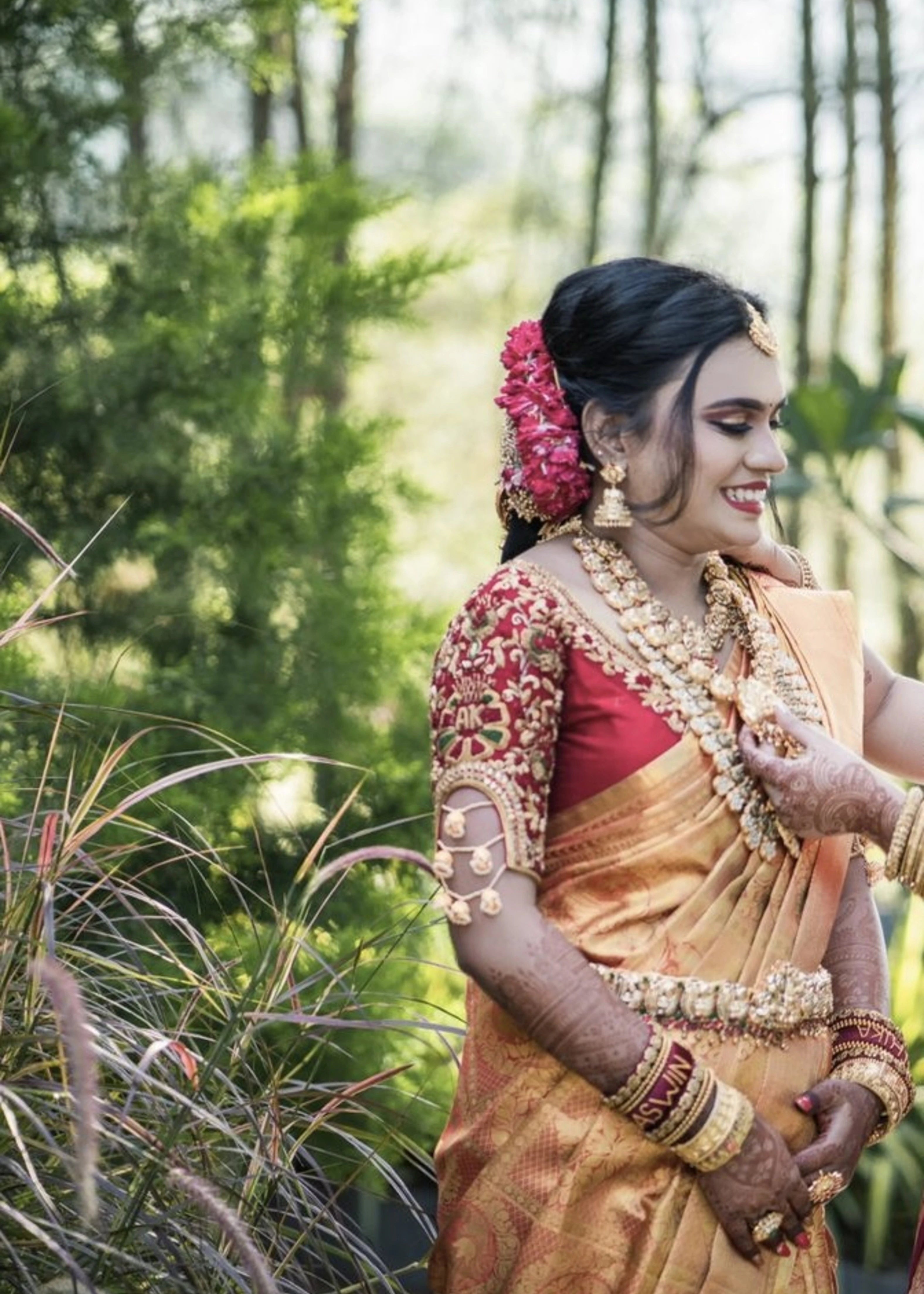 Bride smiling in a red raw silk blouse handcrafted with beads, stones, zardozi, resham knot work and jhumki hangings with creeper motifs designed by Archana Karthick