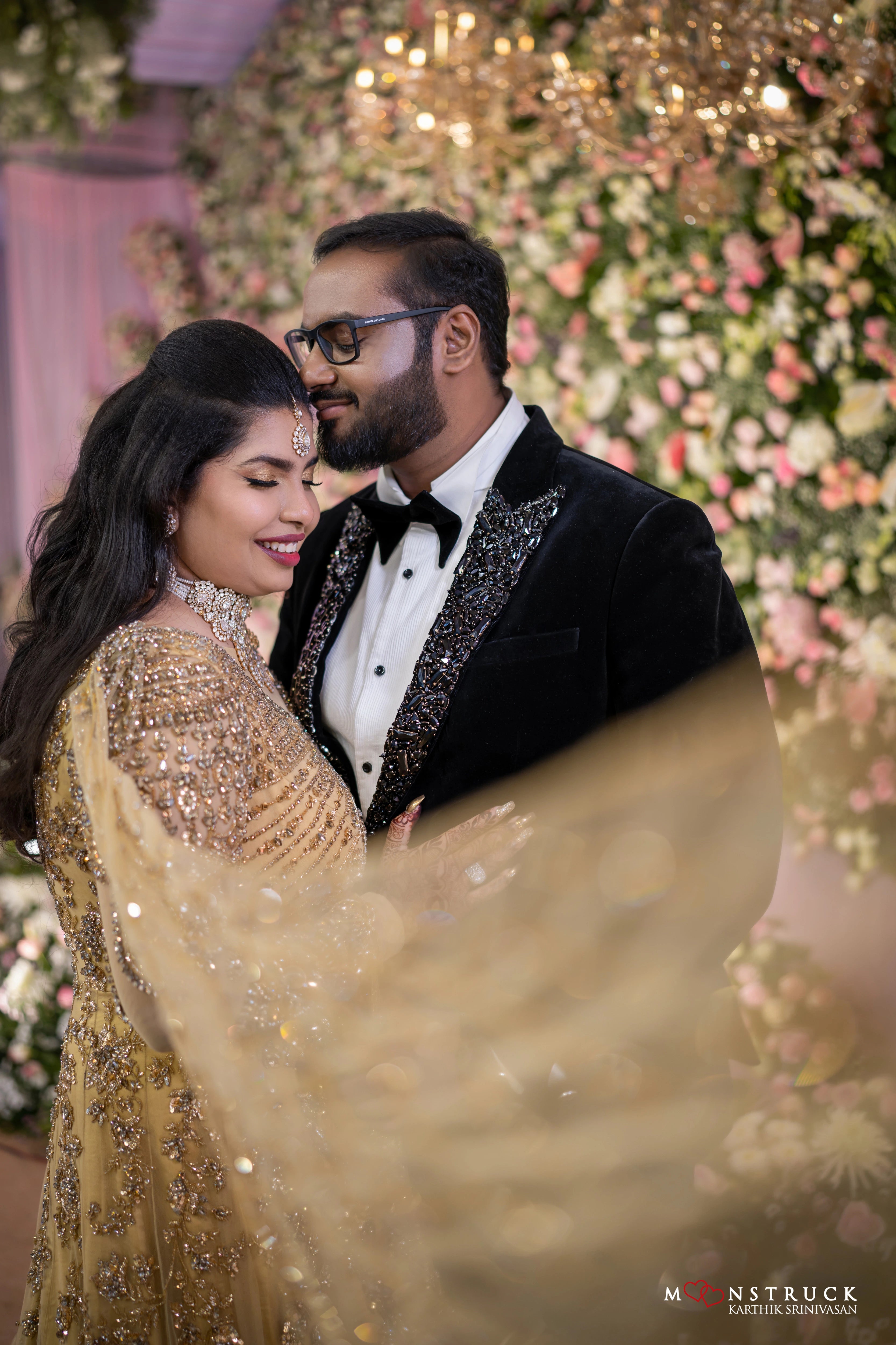 Bride smiling with groom in a gold gown in tulle designed by Archana Karthick and handcrafted with rhinestones and cut dana with floral and geometric motifs.
