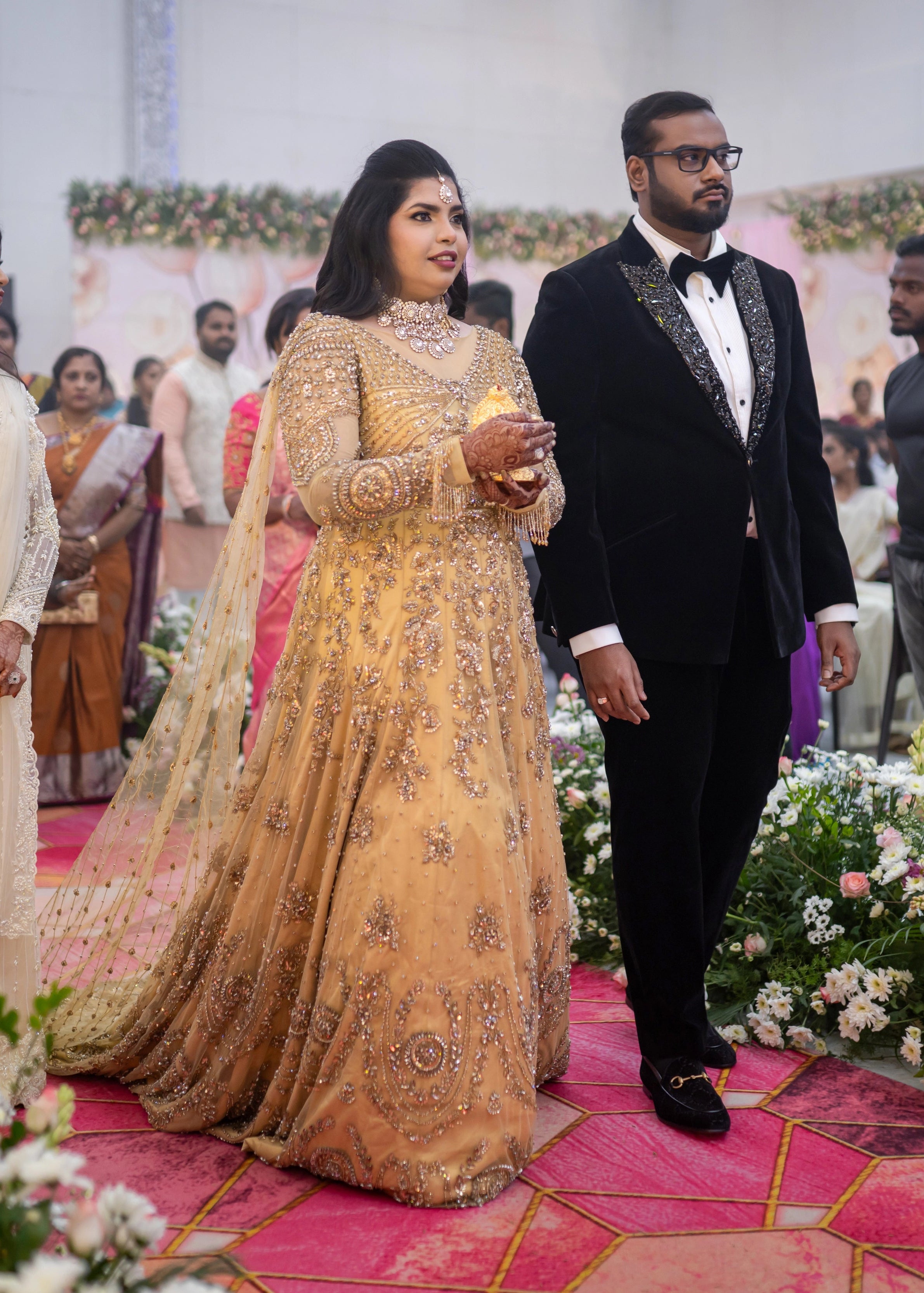 Bride walking down the aisle in a gold gown in tulle designed by Archana Karthick and handcrafted with rhinestones and cut dana with floral and geometric motifs.
