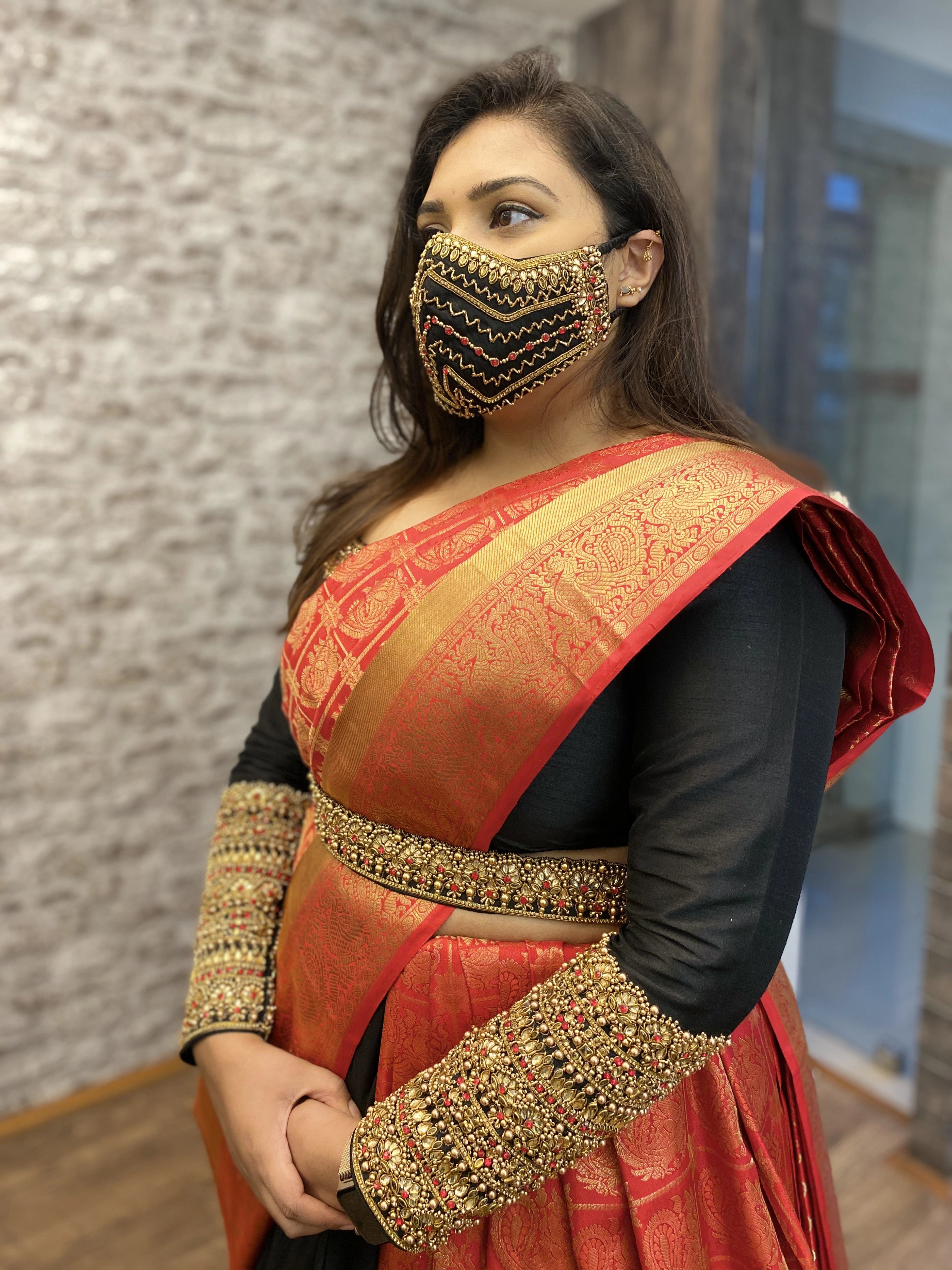 Bridesmaid Nishitha showcasing mask, sleeves and belt in a black and burnt orange half saree, handcrafted with kemp stones, sequins, beads, zardozi and kundan by team Archana Karthick.