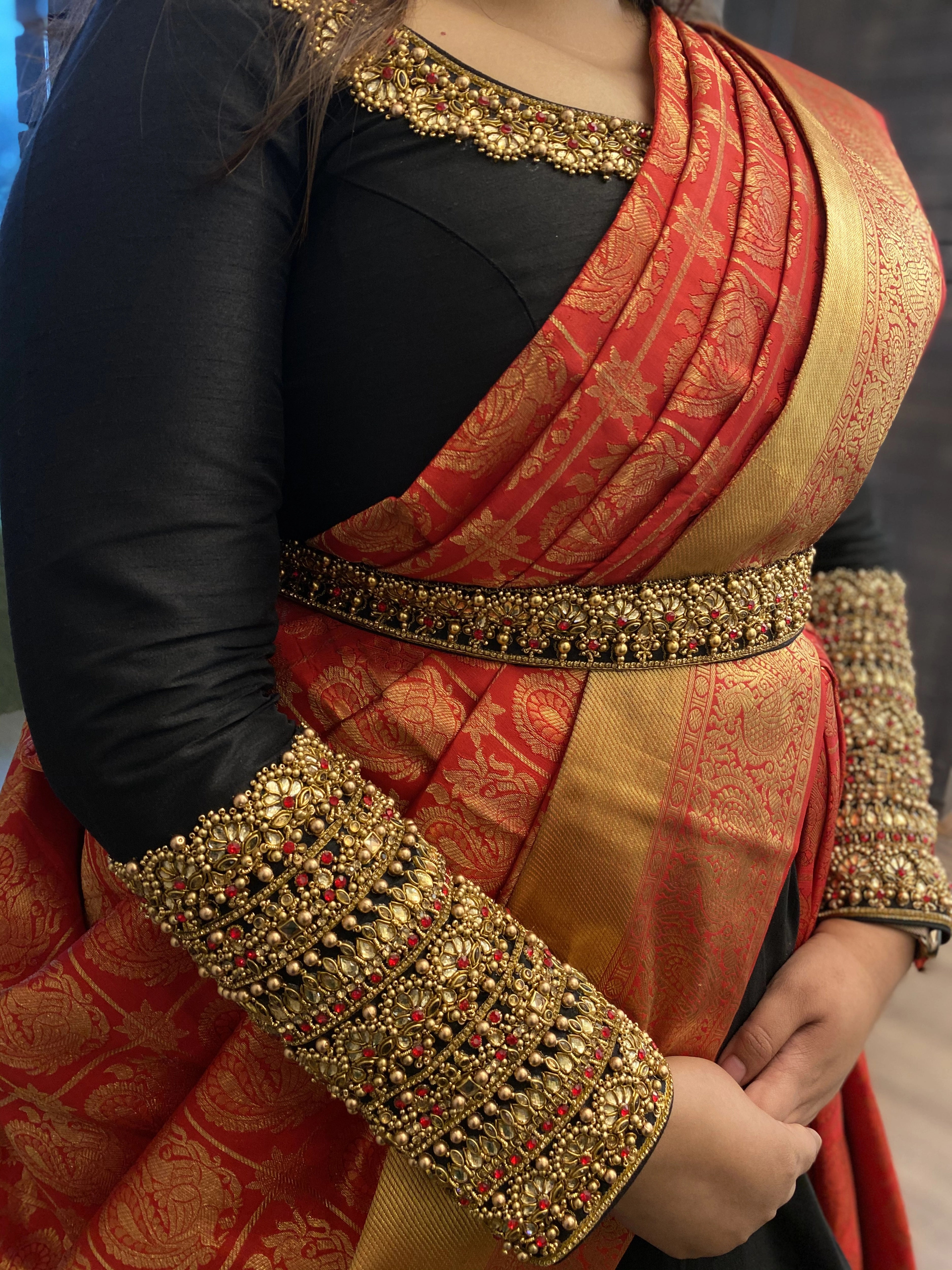Bridesmaid Nishitha showcasing sleeves and belt in a black and burnt orange half saree, handcrafted with kemp stones, sequins, beads, zardozi and kundan by team Archana Karthick.