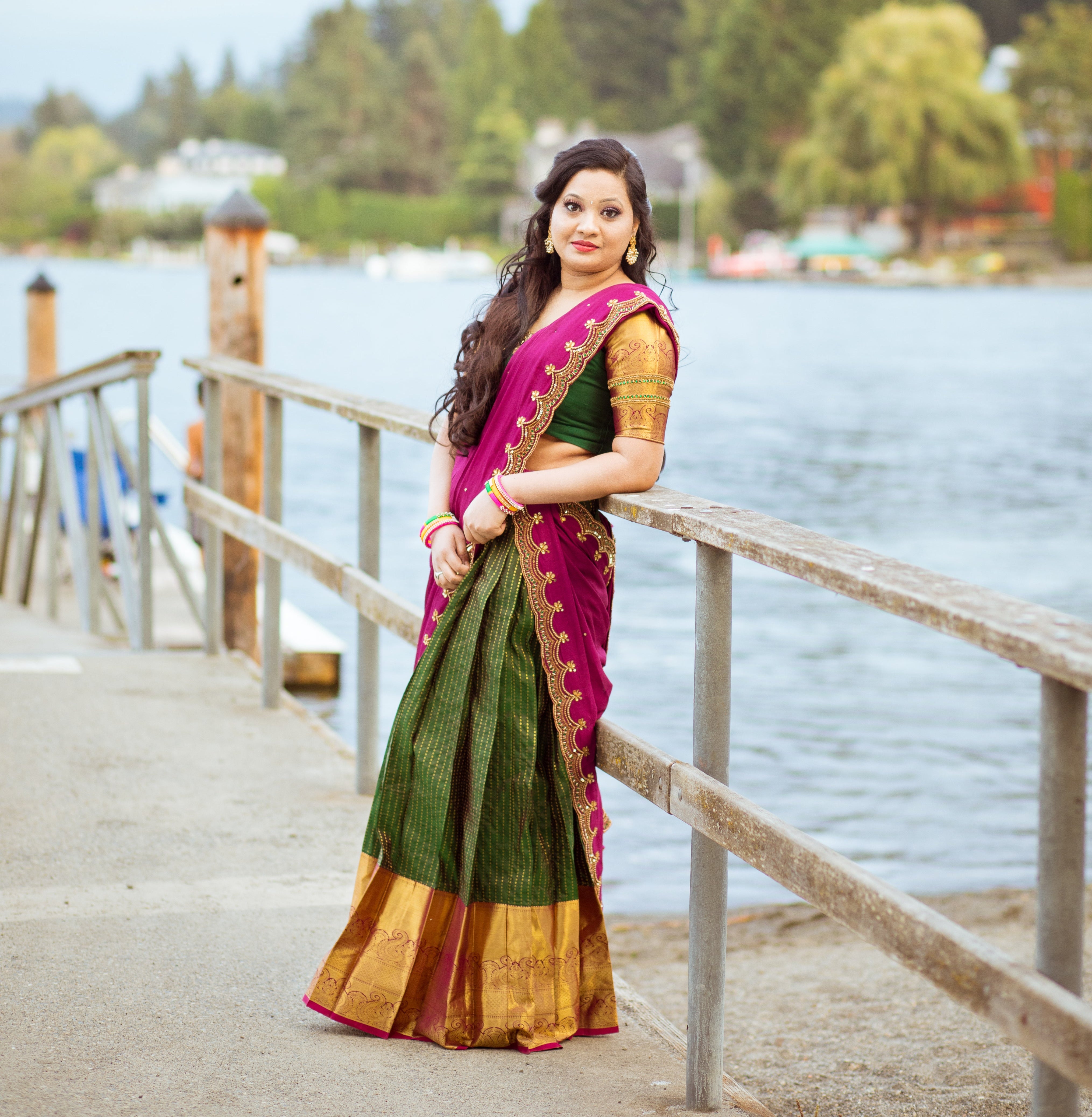 Client, Swathi Pillai, from Seattle leaning on a railing and posing in a bottle green and magenta silk traditional half saree designed by archana karthick.