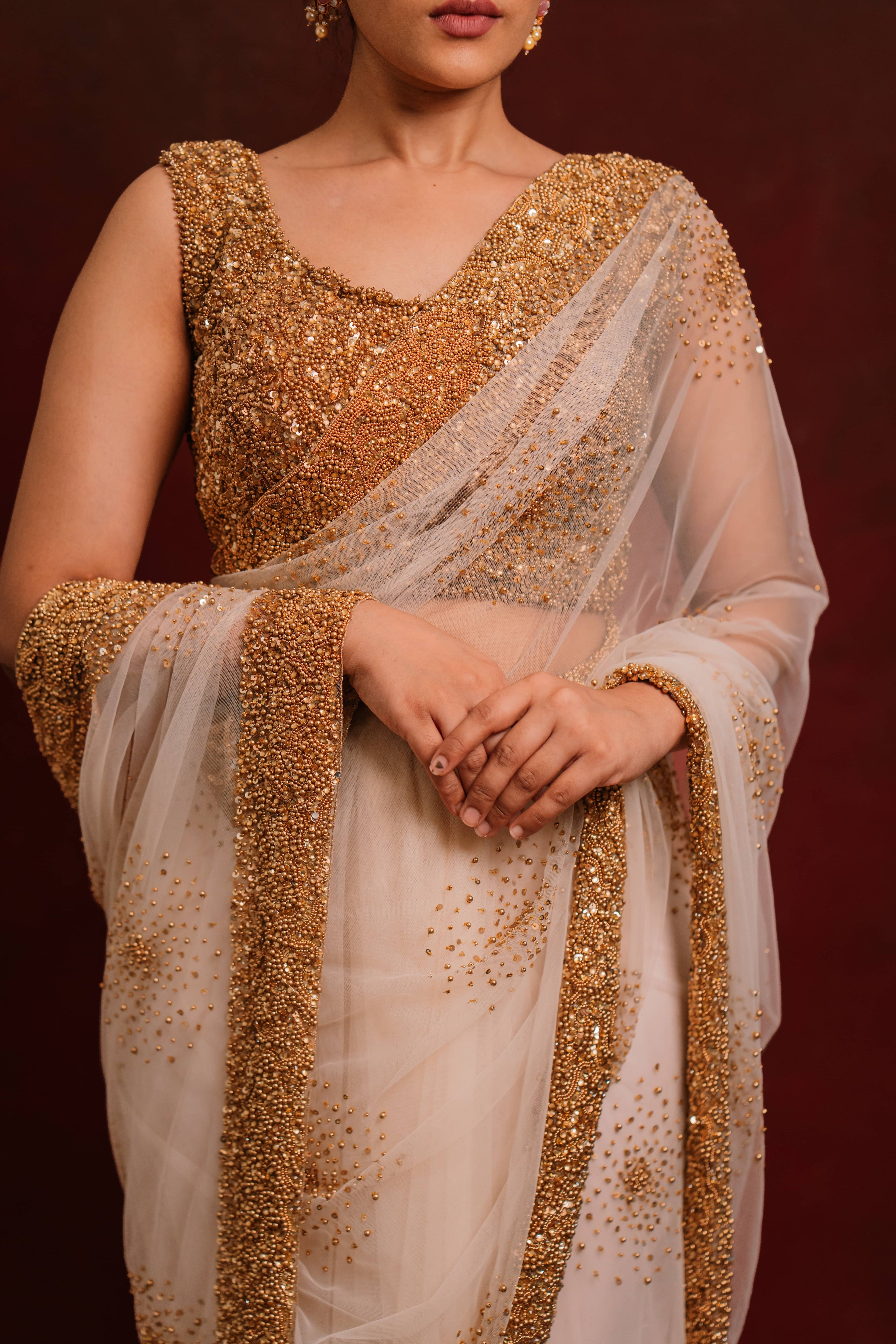 Design details of ivory tulle saree intricately handcrafted with antique gold beads and sequins paired with a handcrafted blouse featuring similar work by team Archana Karthick