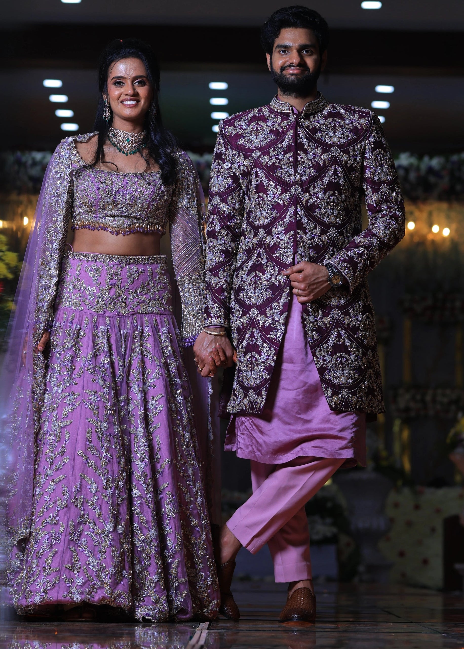 Groom from Canada holding bride's hand in handcrafted purple sherwani by Archana Karthick