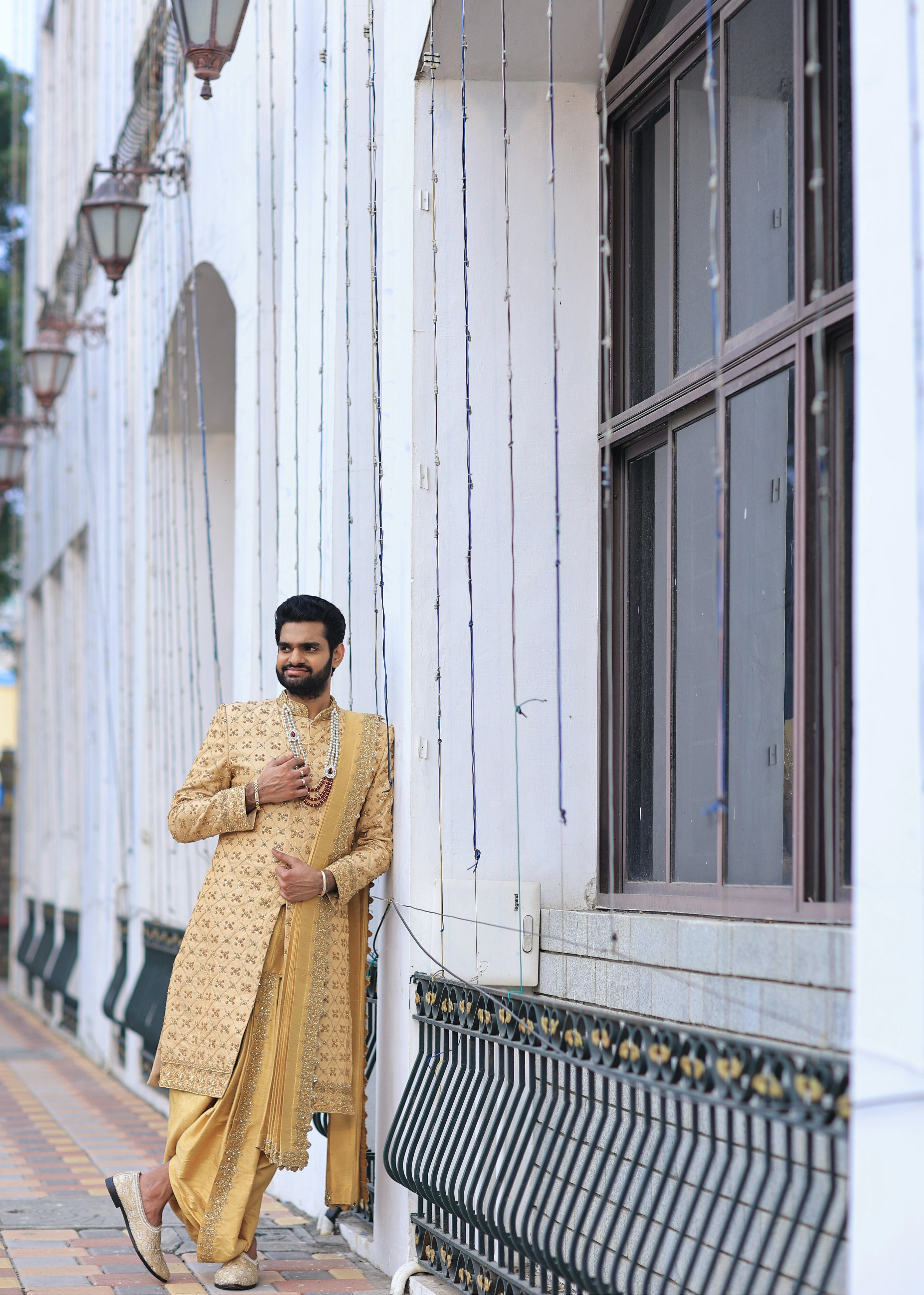 Groom from Canada leaning in handcrafted gold sherwani by Archana Karthick