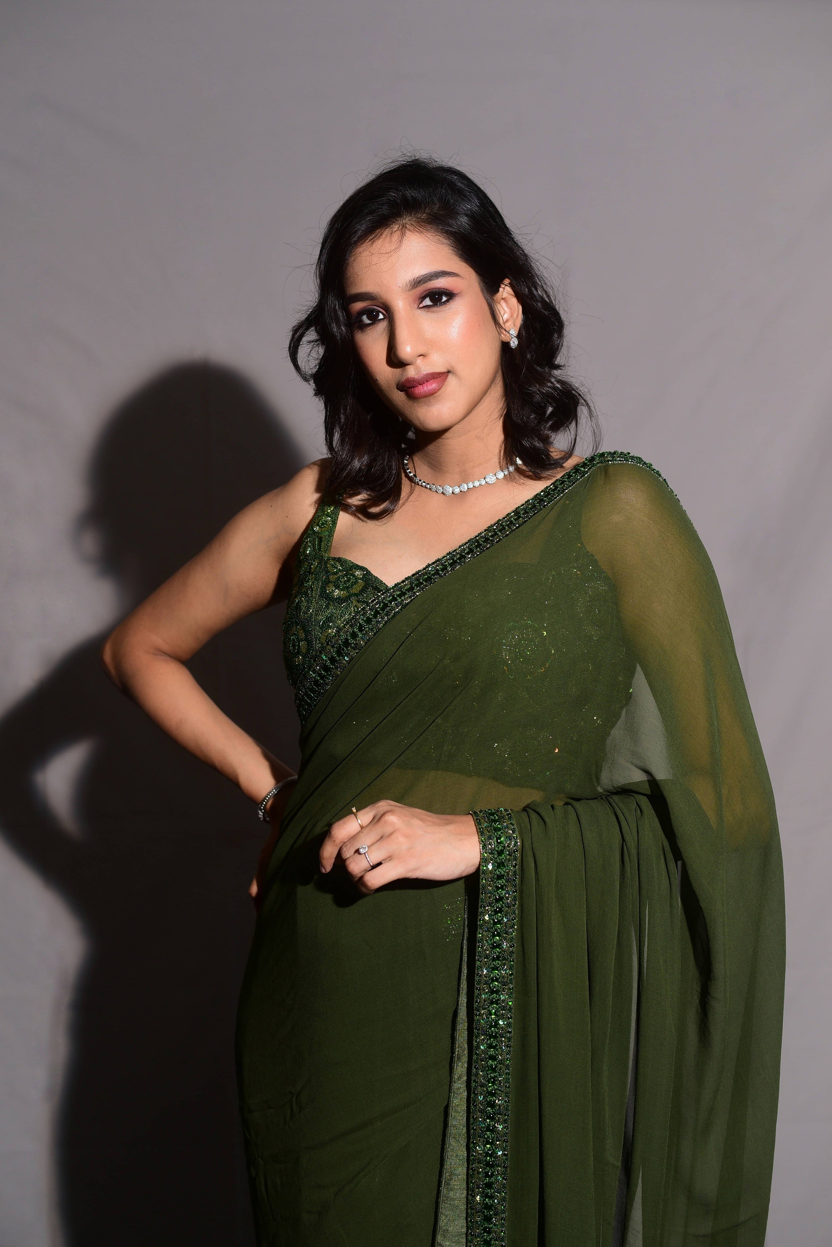 Influencer & Model Ashwini Kumar smiling in a moss Green georgette saree paired with a heavily embellished bralette from the Lo-Mance Collection by Archana Karthick.