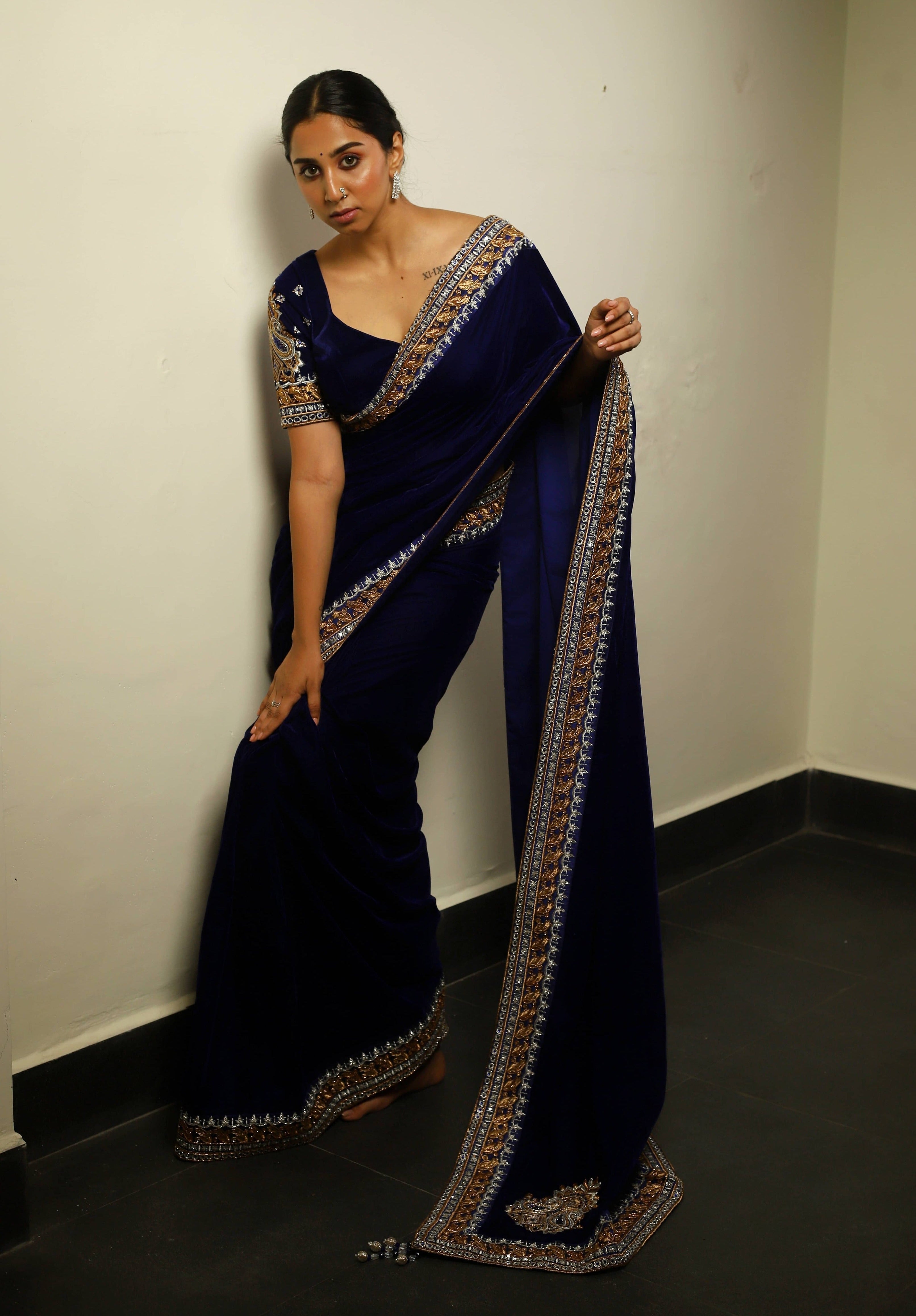 Influencer Deekshita Nikkam in a navy velvet saree and blouse set with zardozi detailings on border and sleeves. Bent forward pose.
