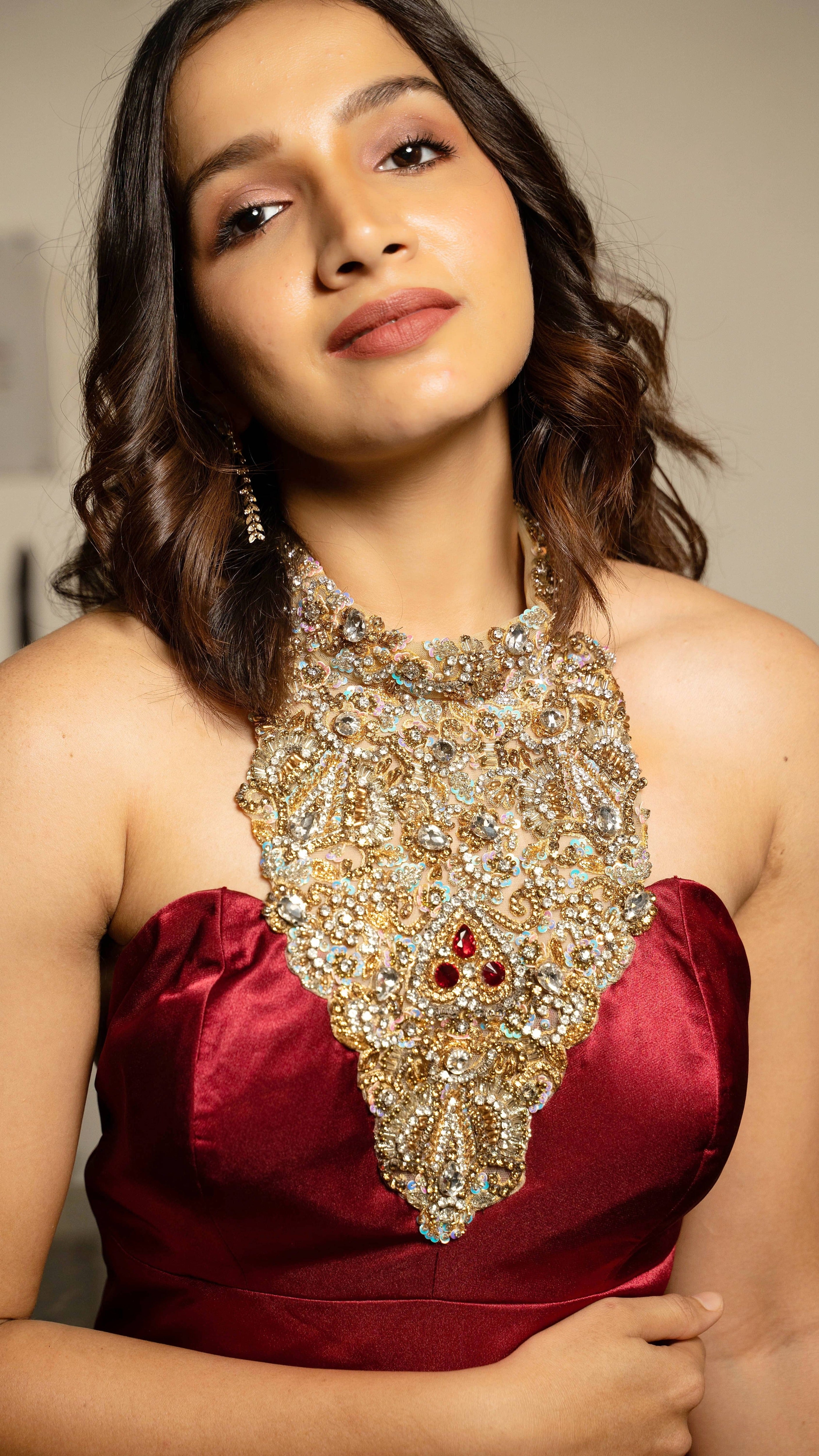 Influencer and actress Shweta Gai in a red satin silk halterneck gown with a heavily embellished neckline. Looking at the camera with a smile.