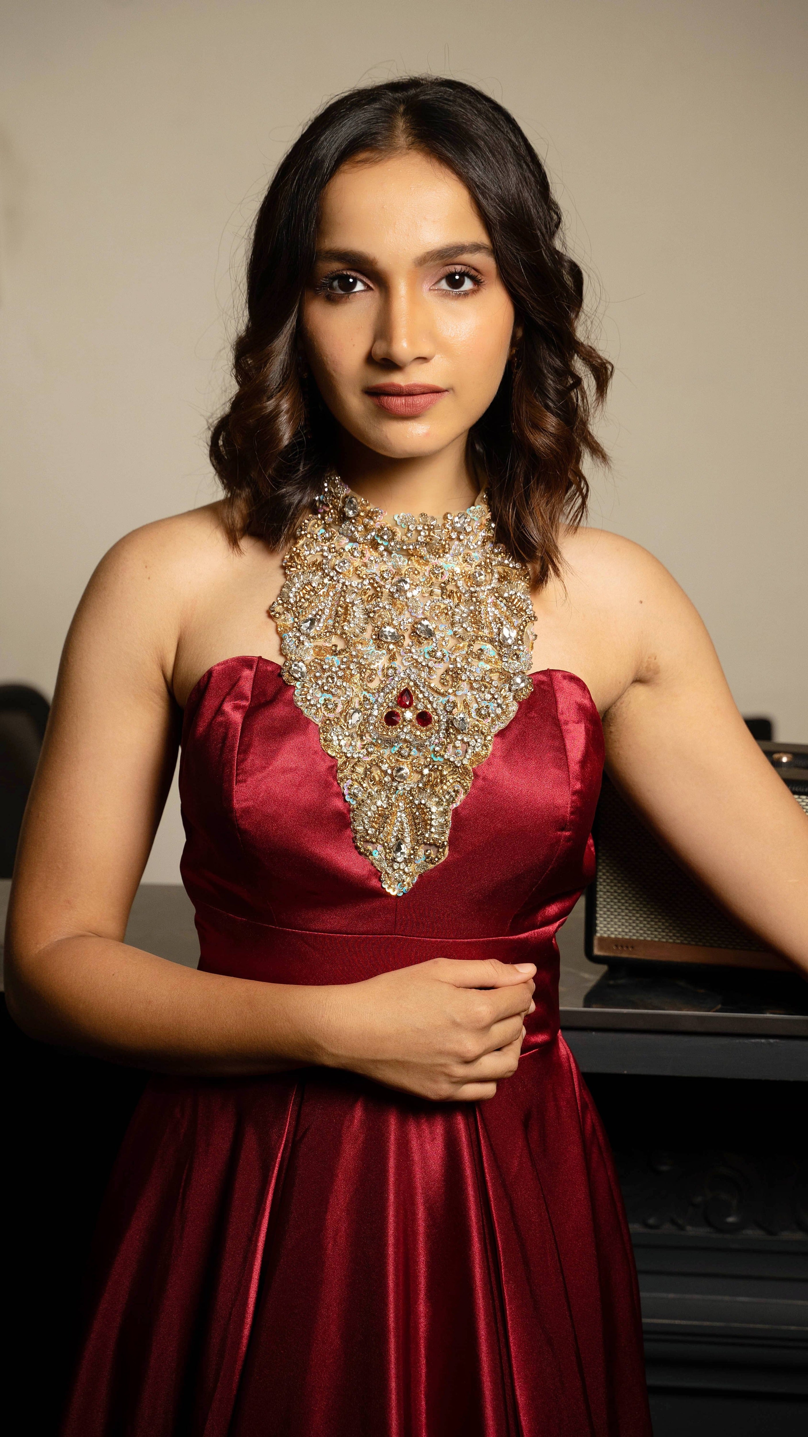 Influencer and actress Shweta Gai in a red satin silk halterneck gown with a heavily embellished neckline. Looking straight at the camera.