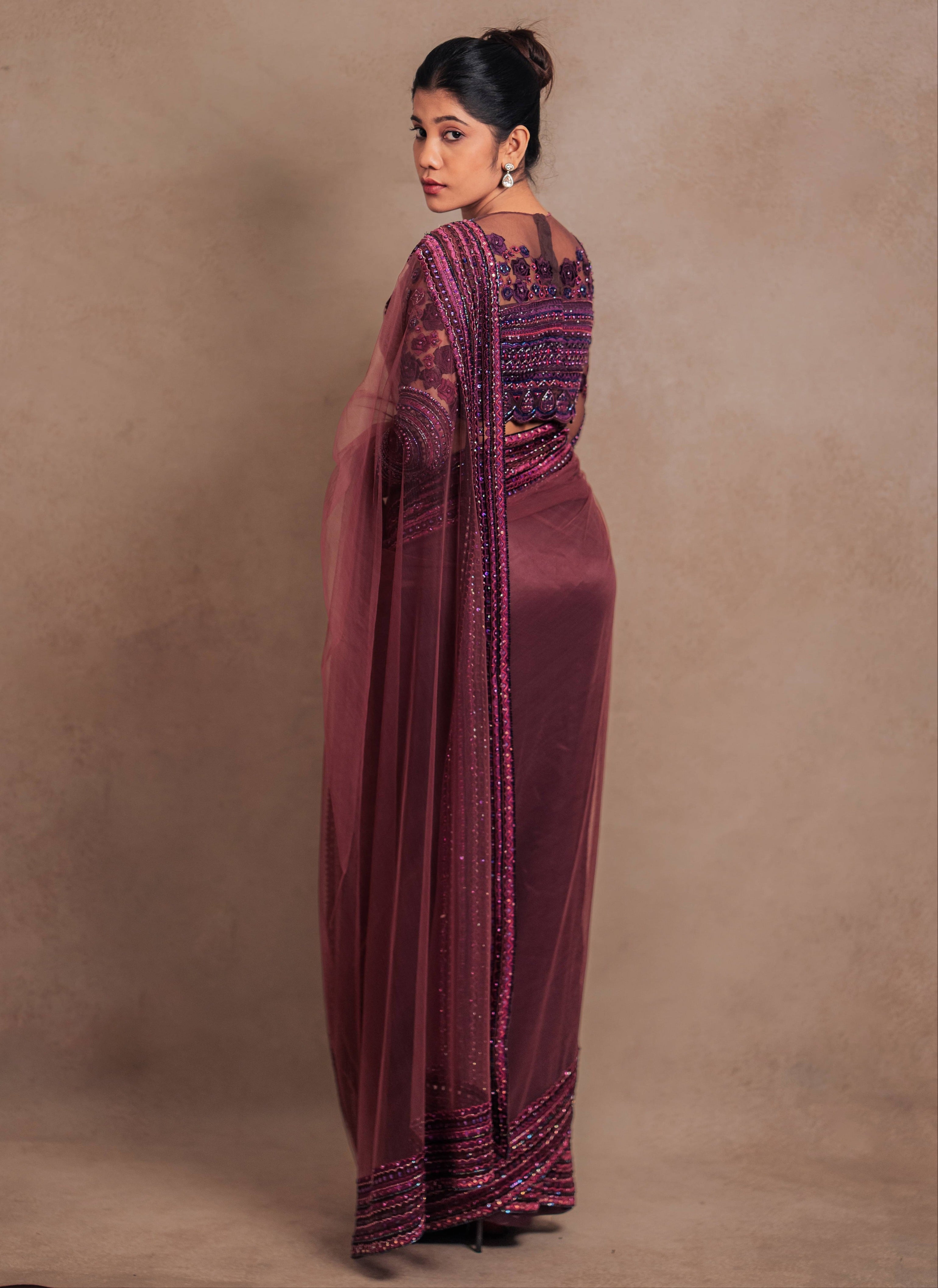 Jaina Parmar, known for recreating looks of actress Nayanthara is seen here in a purple net saree with heavily embellished border and full sleeved blouse with stone and resham work posing for full back design