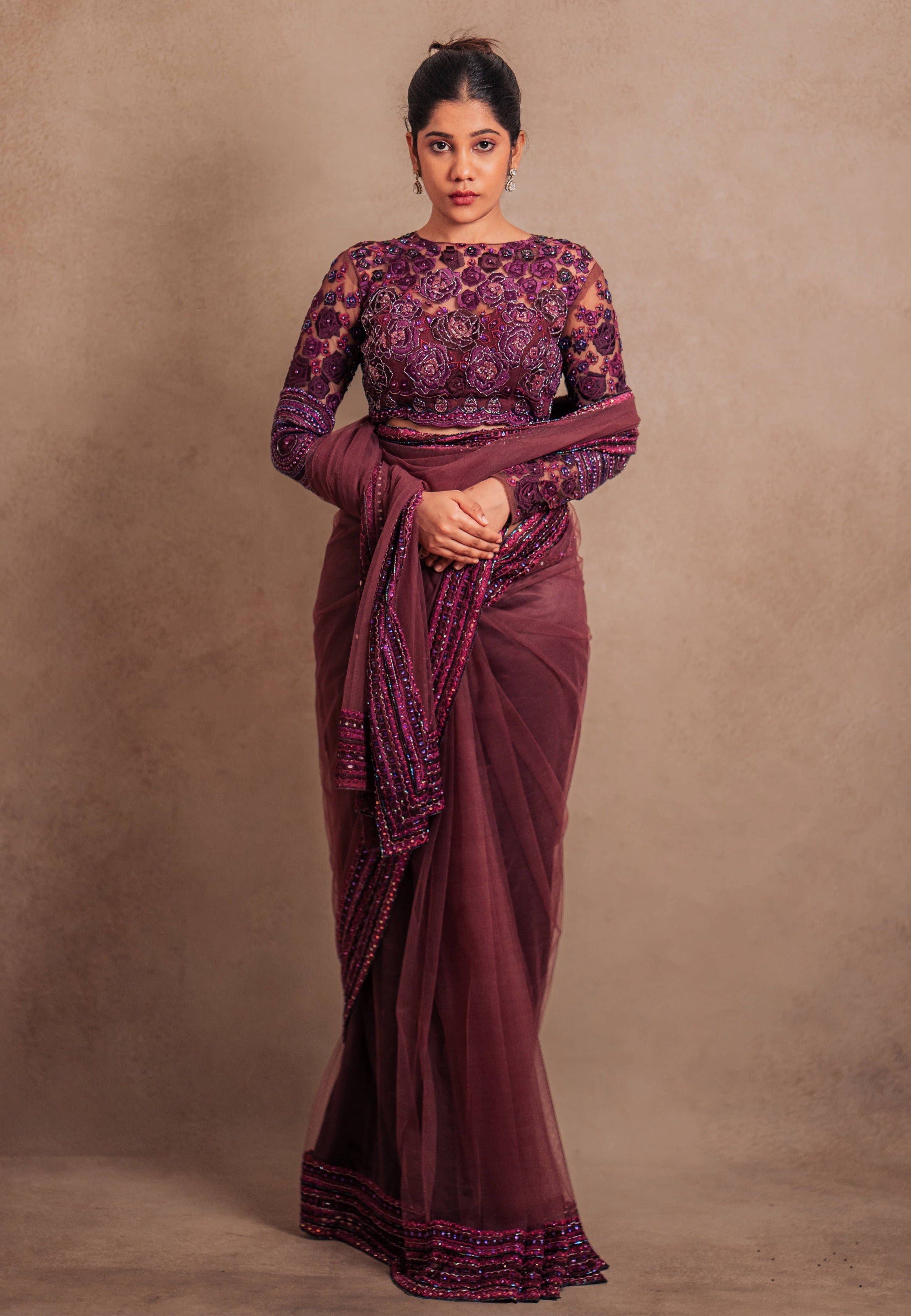 Jaina Parmar, known for recreating looks of actress Nayanthara is seen here in a purple net saree with heavily embellished border and full sleeved blouse with stone and resham work posing for full front profile