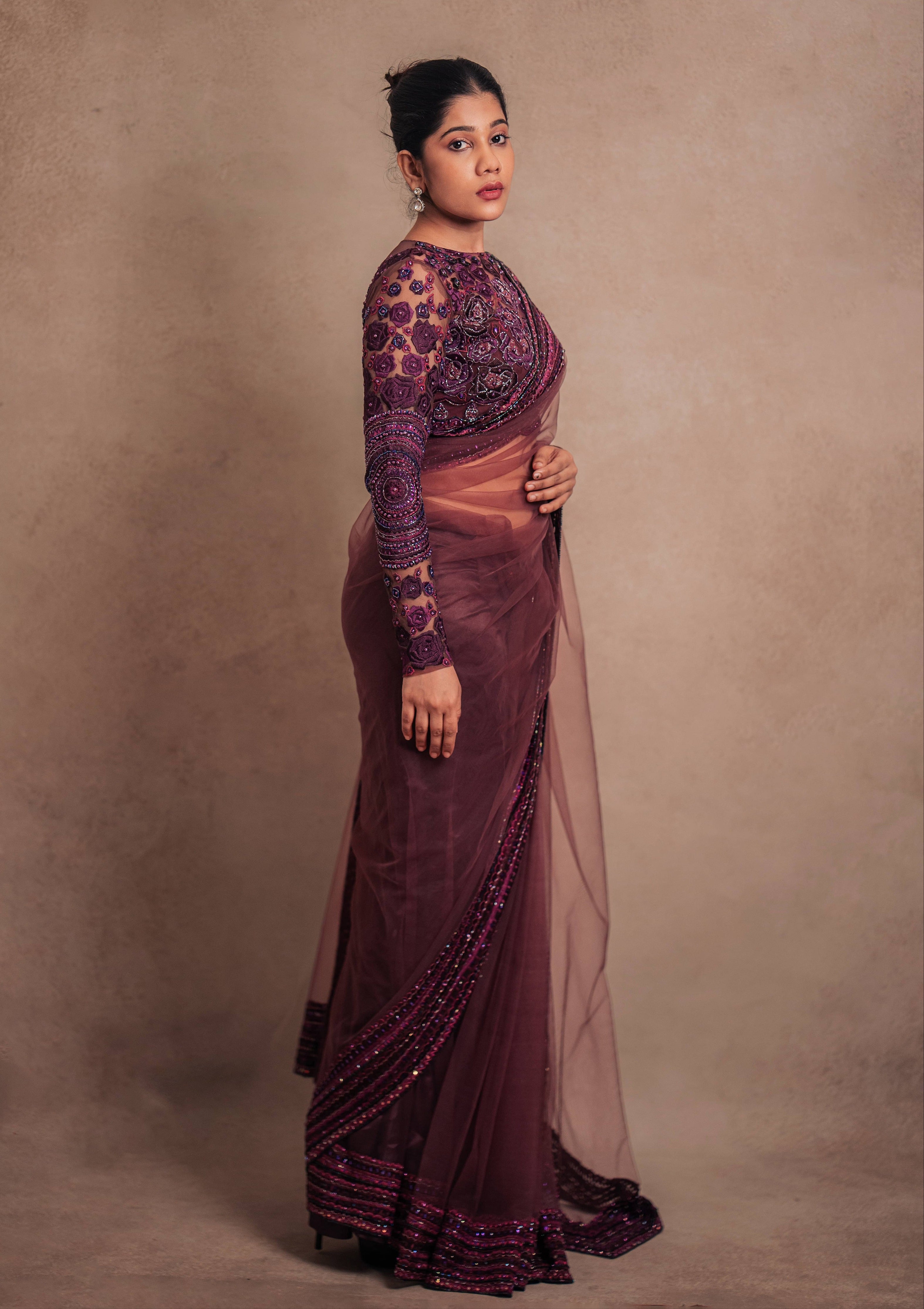 Jaina Parmar, known for recreating looks of actress Nayanthara is seen here in a purple net saree with heavily embellished border and full sleeved blouse with stone and resham work posing for full side profile of sleeve and saree
