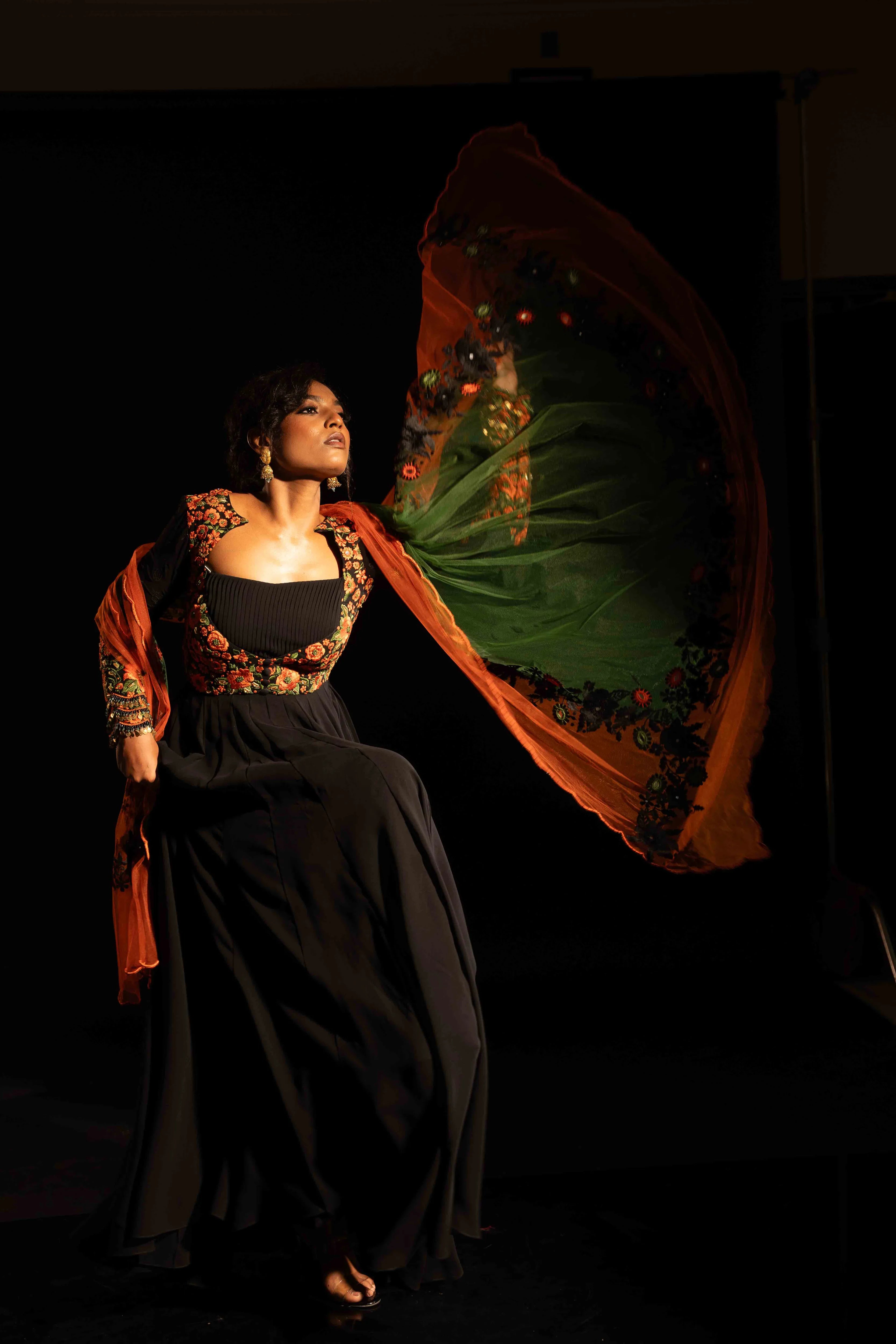 Model Ashika in a black anarkali with an orange green dupatta, handcrafted with resham, mirror and metal coins for "HAZE" - A/W'25 capsule collection by Archana Karthick.