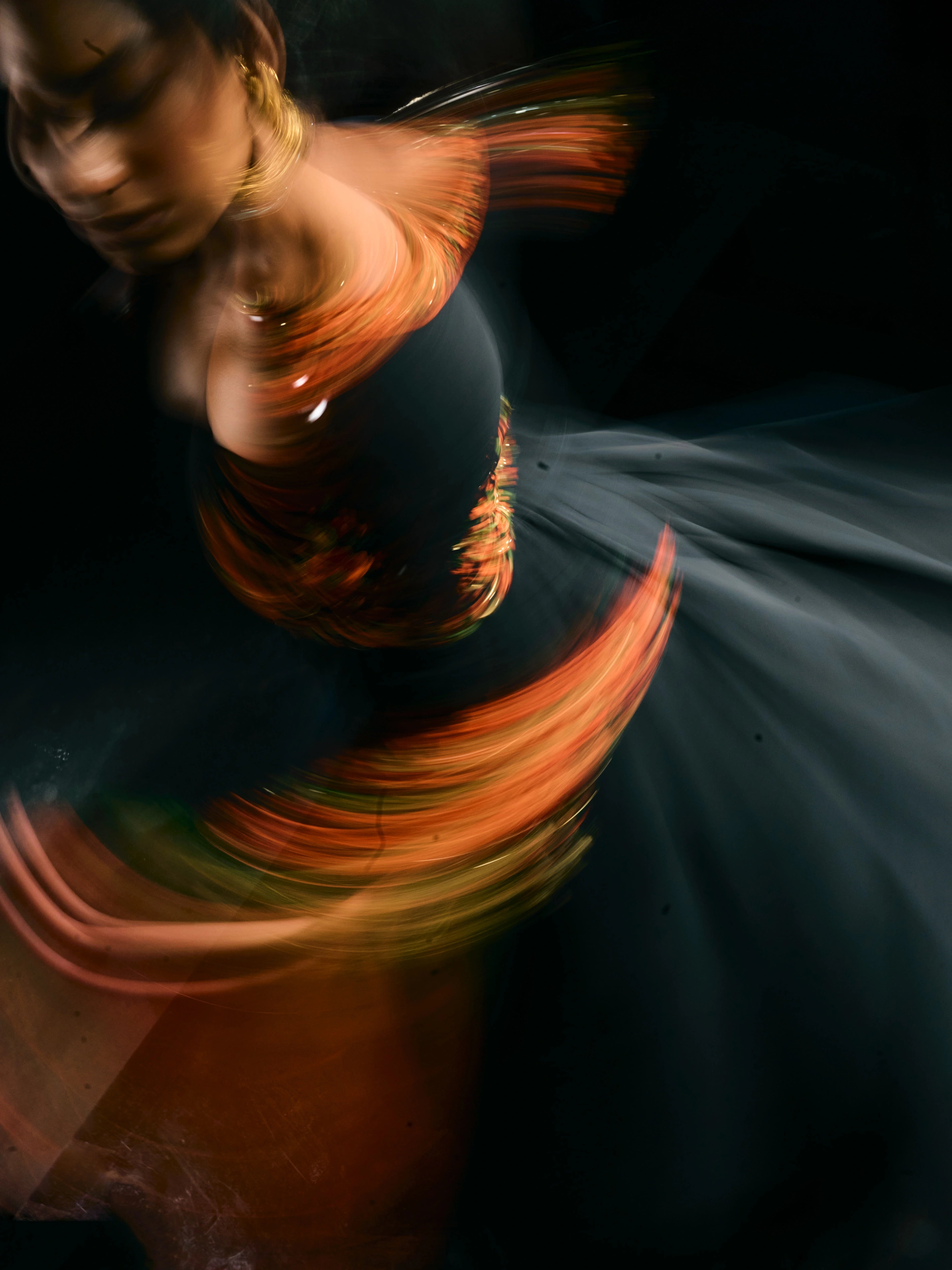 Model Ashika posing for a blurred shot in a black anarkali with an orange green dupatta, handcrafted with resham, mirror and metal coins for "HAZE" - A/W'25 capsule collection by Archana Karthick.