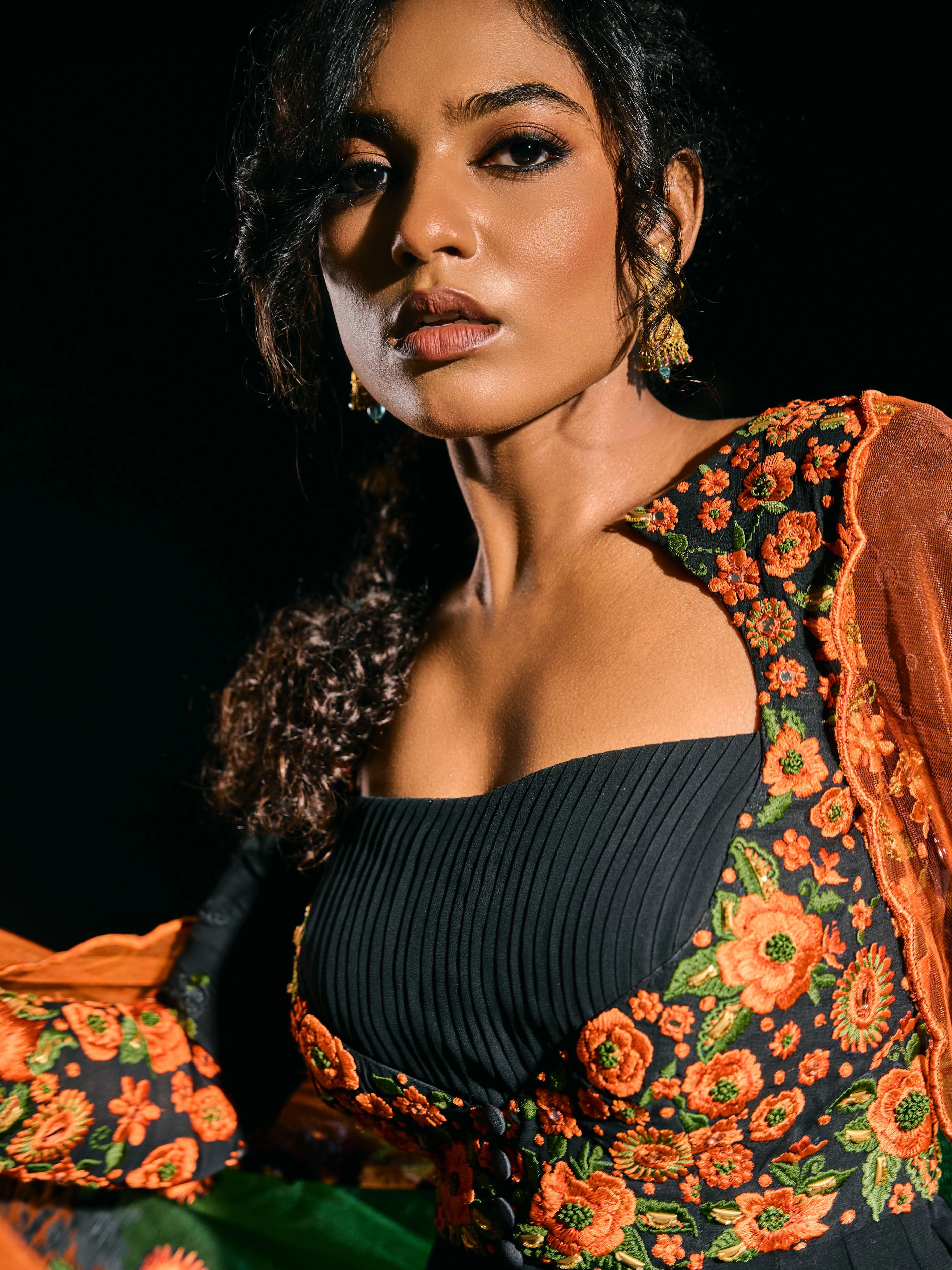 Model Ashika posing for closeup in a black anarkali with an orange green dupatta, handcrafted with resham, mirror and metal coins for "HAZE" - A/W'25 capsule collection by Archana Karthick.