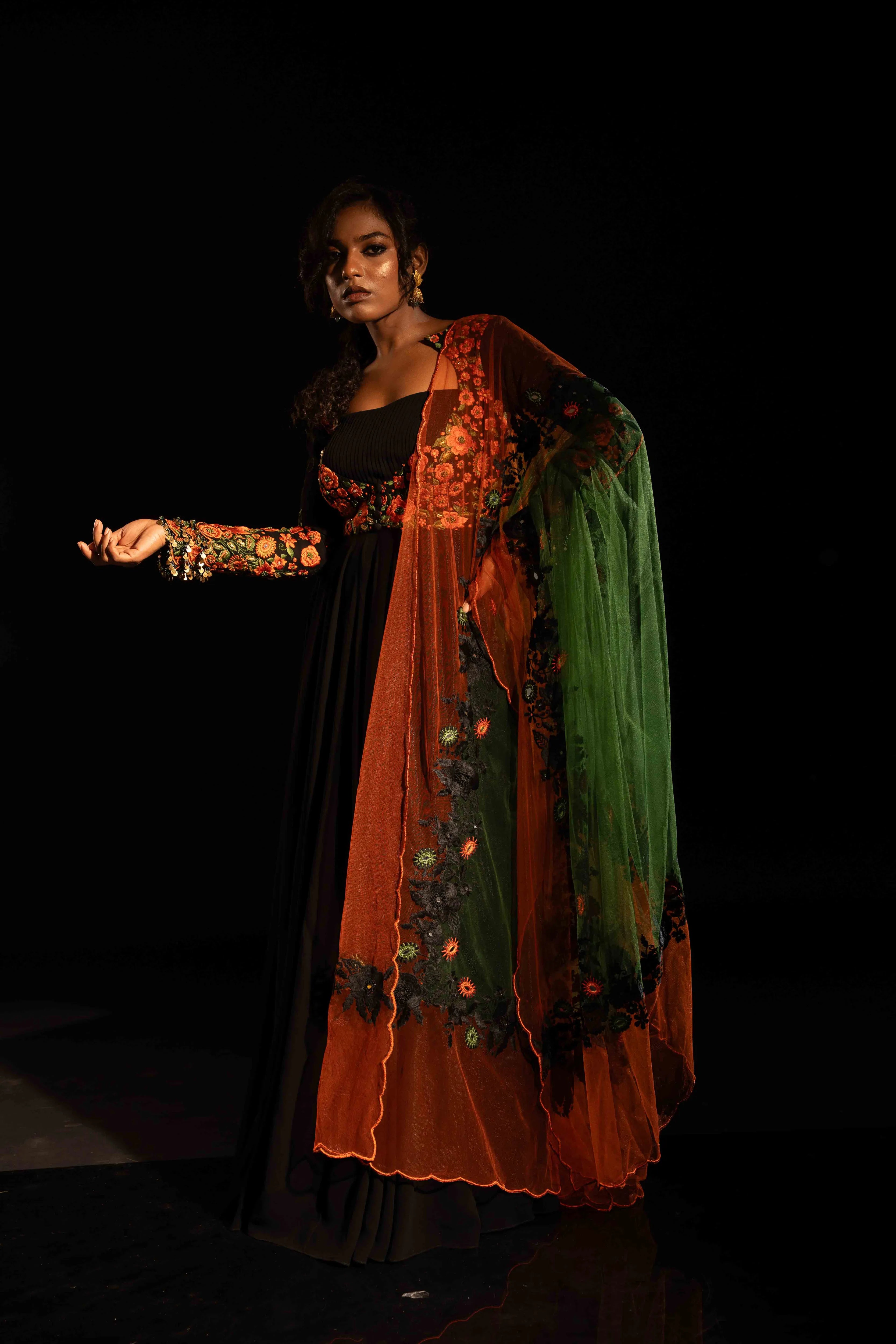 Model Ashika posing in a black anarkali with an orange green dupatta, handcrafted with resham, mirror and metal coins for "HAZE" - A/W'25 capsule collection by Archana Karthick.