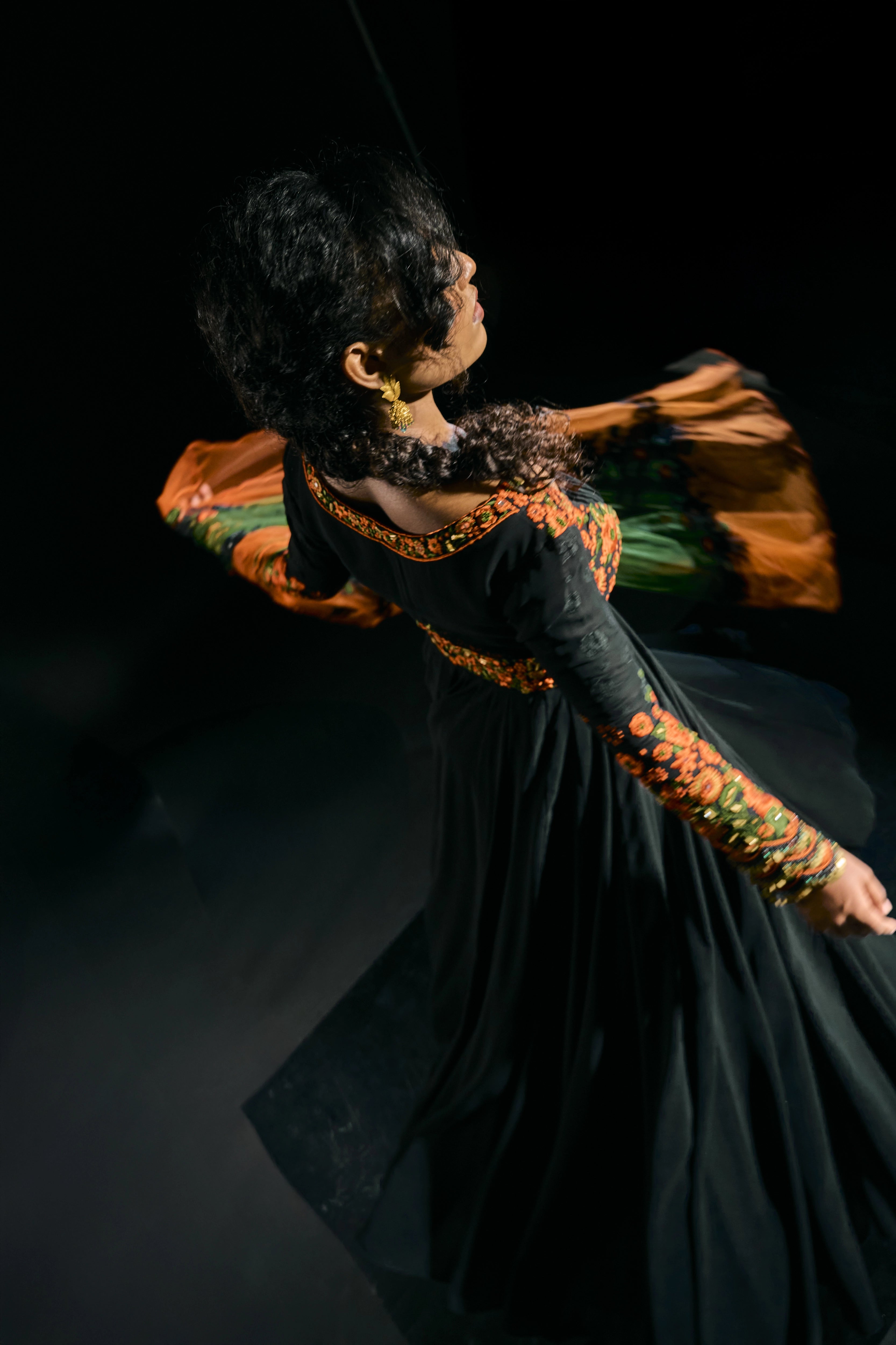 Model Ashika twirling in a black anarkali with an orange green dupatta, handcrafted with resham, mirror and metal coins for "HAZE" - A/W'25 capsule collection by Archana Karthick.