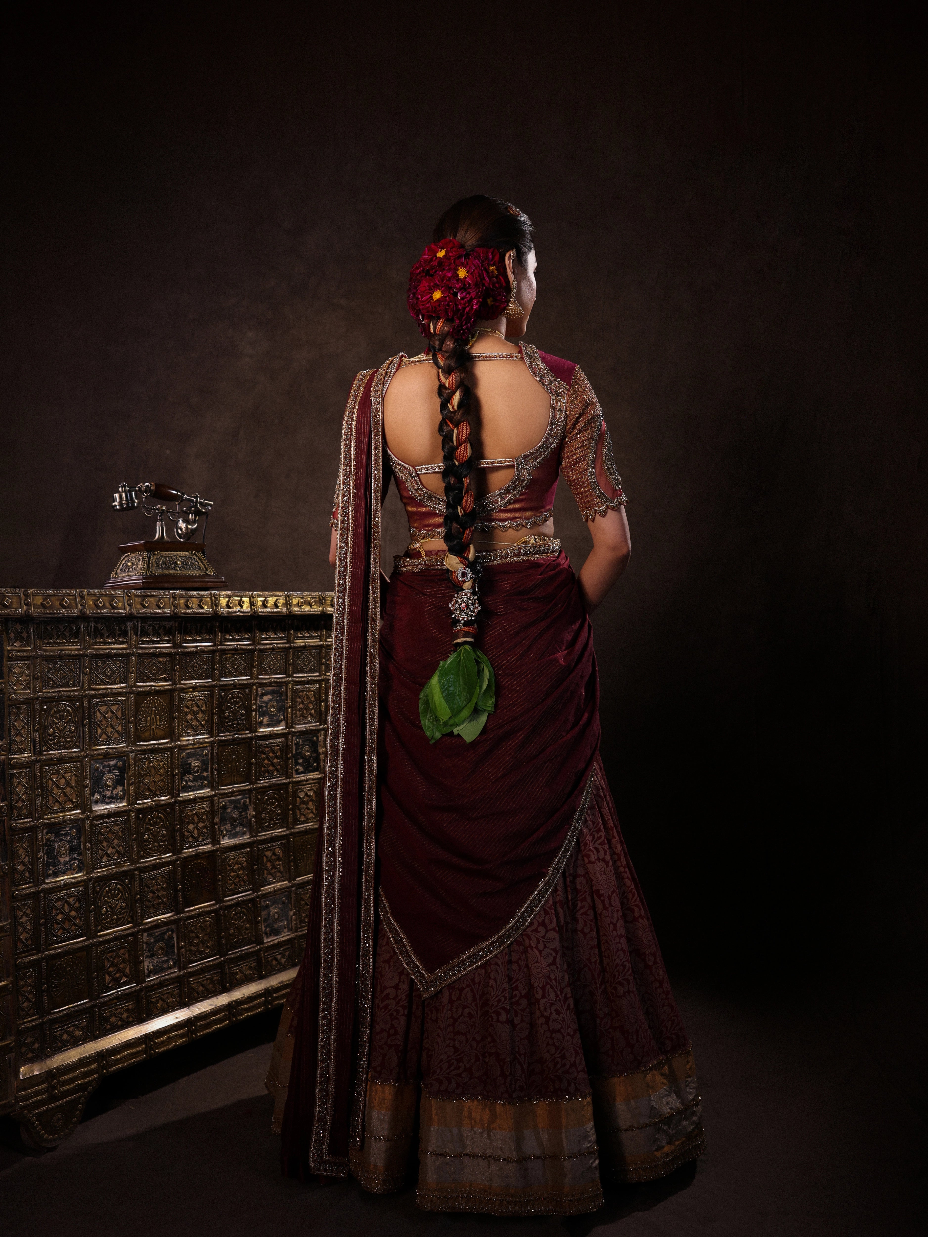 Model Dr Sree Advaita showcasing back design in a brownish maroon silk half saree set intricately handcrafted with zardozi, resham, cutdana, sequins & rhinestones. Team Archana Karthick completed the style with maroon glass bangles, a ring, jhumkas, nose ring and a maang tikka.