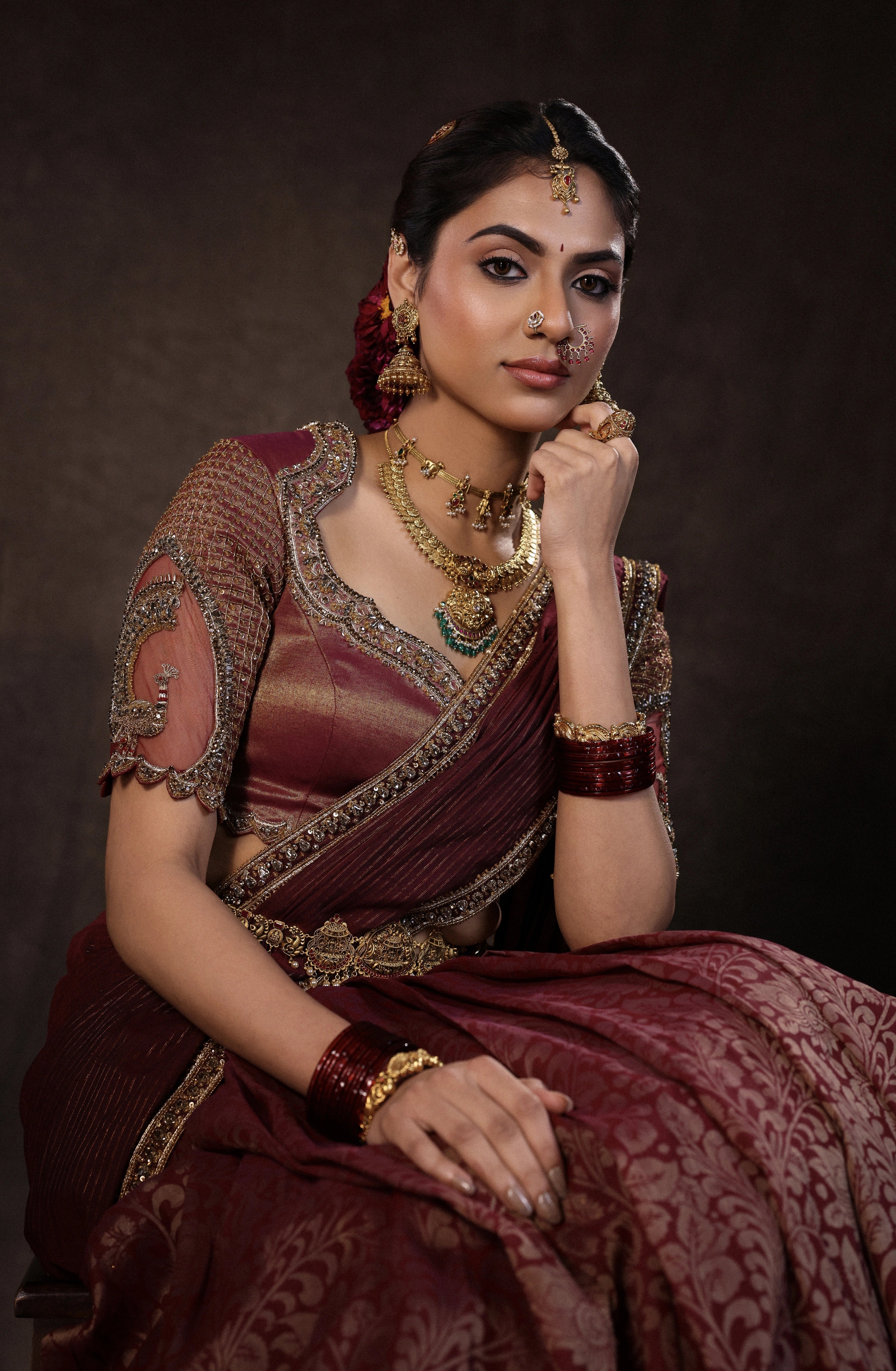 Model Dr Sree Advaita smiles in a brownish maroon silk half saree set intricately handcrafted with zardozi, resham, cutdana, sequins & rhinestones. Team Archana Karthick completed the style with maroon glass bangles, a ring, jhumkas, nose ring and a maang tikka.