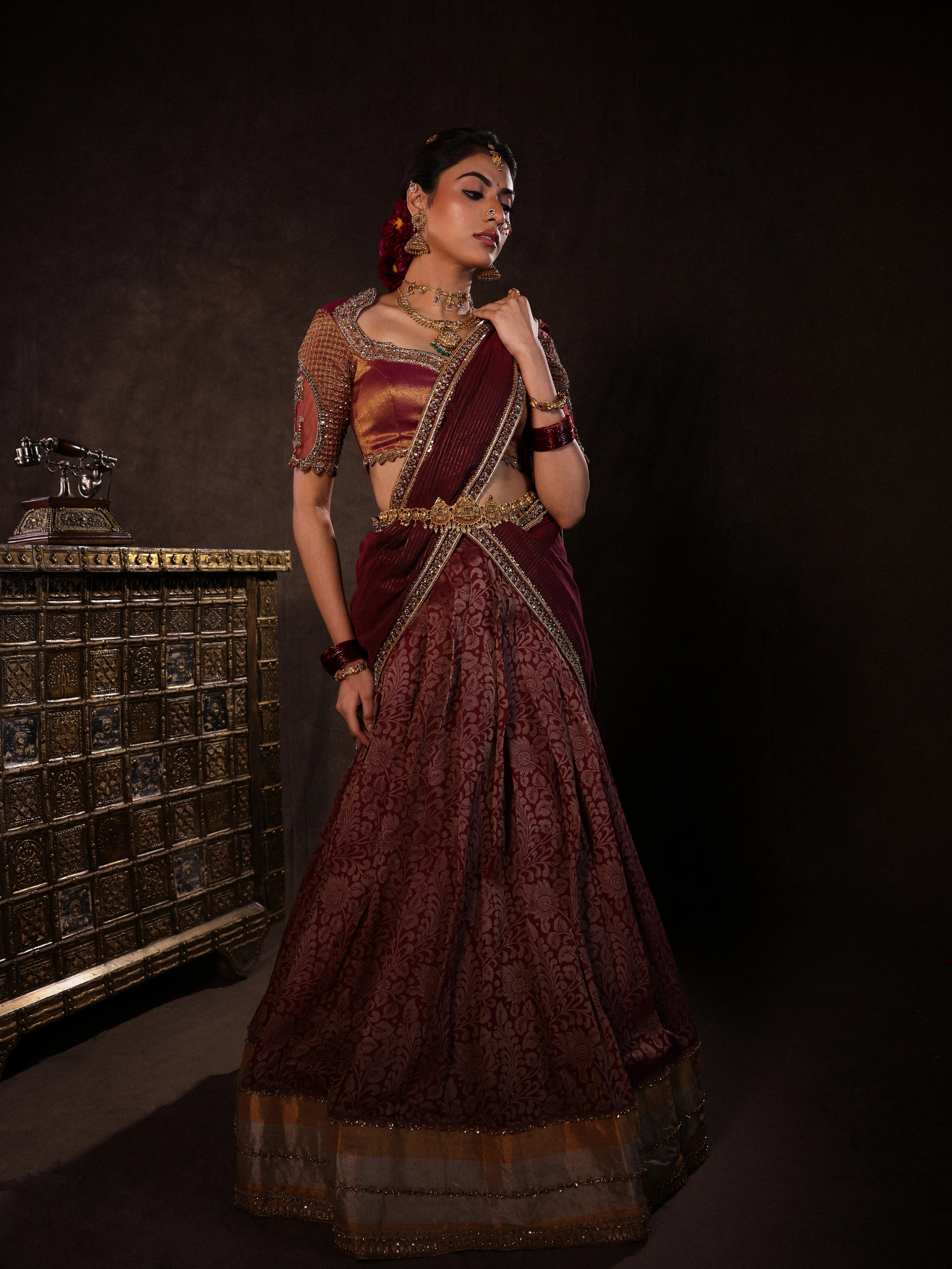 Model Dr Sree Advaita strikes a pose in a brownish maroon silk half saree set intricately handcrafted with zardozi, resham, cutdana, sequins & rhinestones. Team Archana Karthick completed the style with maroon glass bangles, a ring, jhumkas, nose ring and a maang tikka.