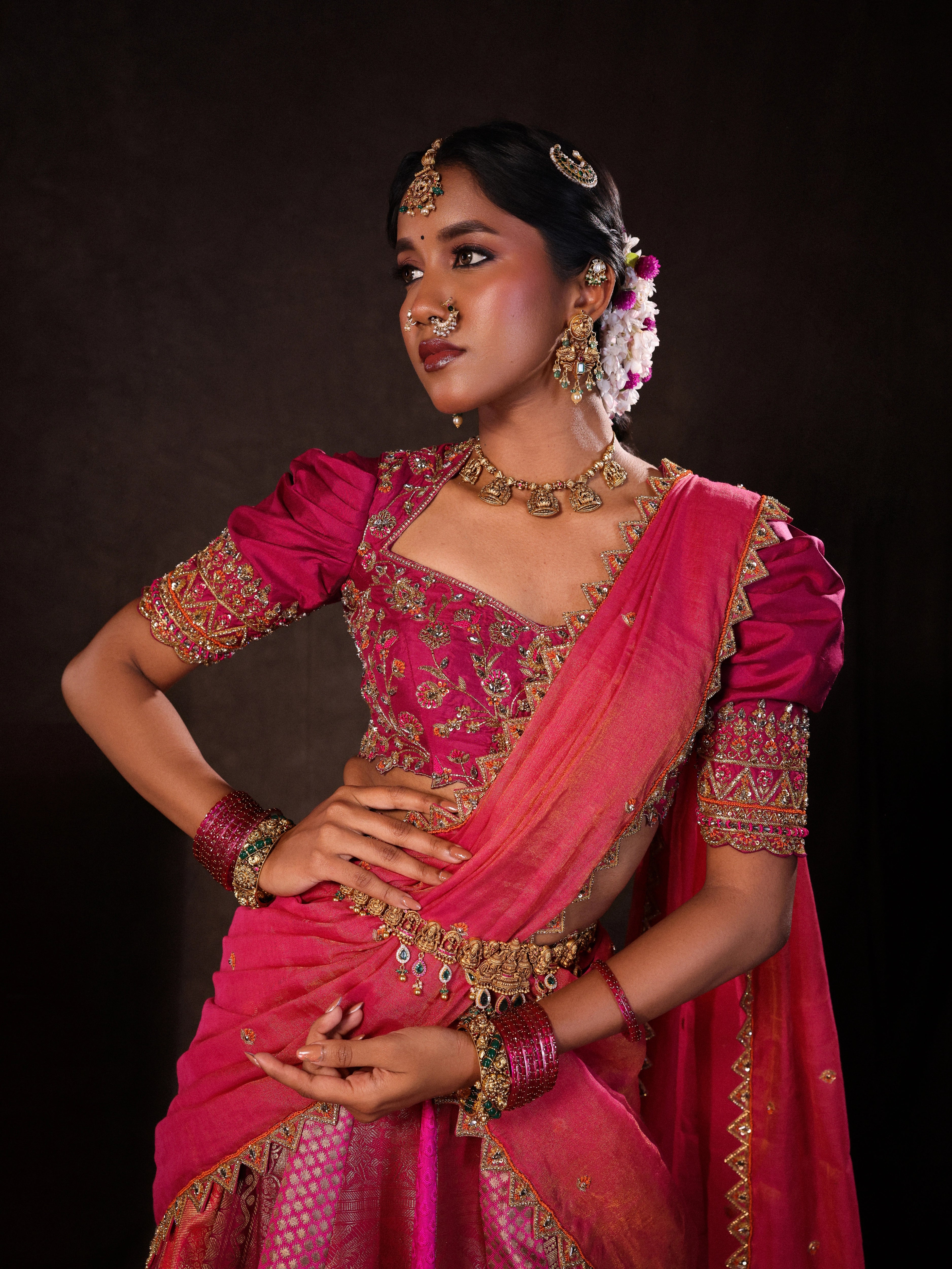Model Gayathri Dhanasekar poses during photoshoot in a pink & orange silk half saree handcrafted with zardozi, cutdana (bugle beads), resham (silk thread), sequins and rhinestones. Team Archana Karthick completed the style with pink glass bangles, a ring, a choker, jhumkas, nose ring and a maang tikka.