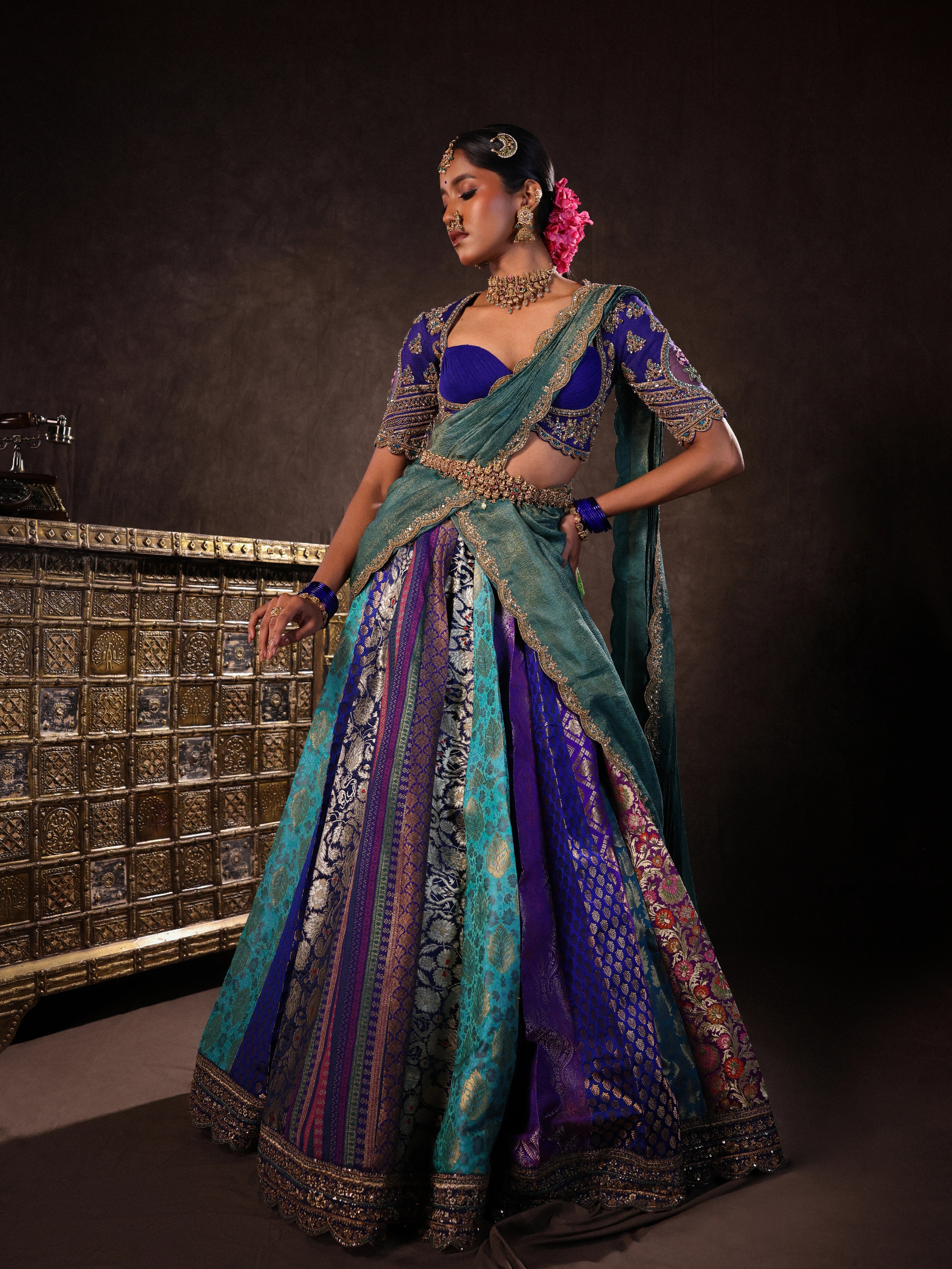 Model Gayathri Dhanasekar posing in a brocade, raw silk and tissue silk half saree set in shades of blue handcrafted with zardozi, resham, sequins and rhinestones. Team Archana Karthick completed the style with blue glass bangles, a ring, a choker, jhumkas, nose ring and a maang tikka.