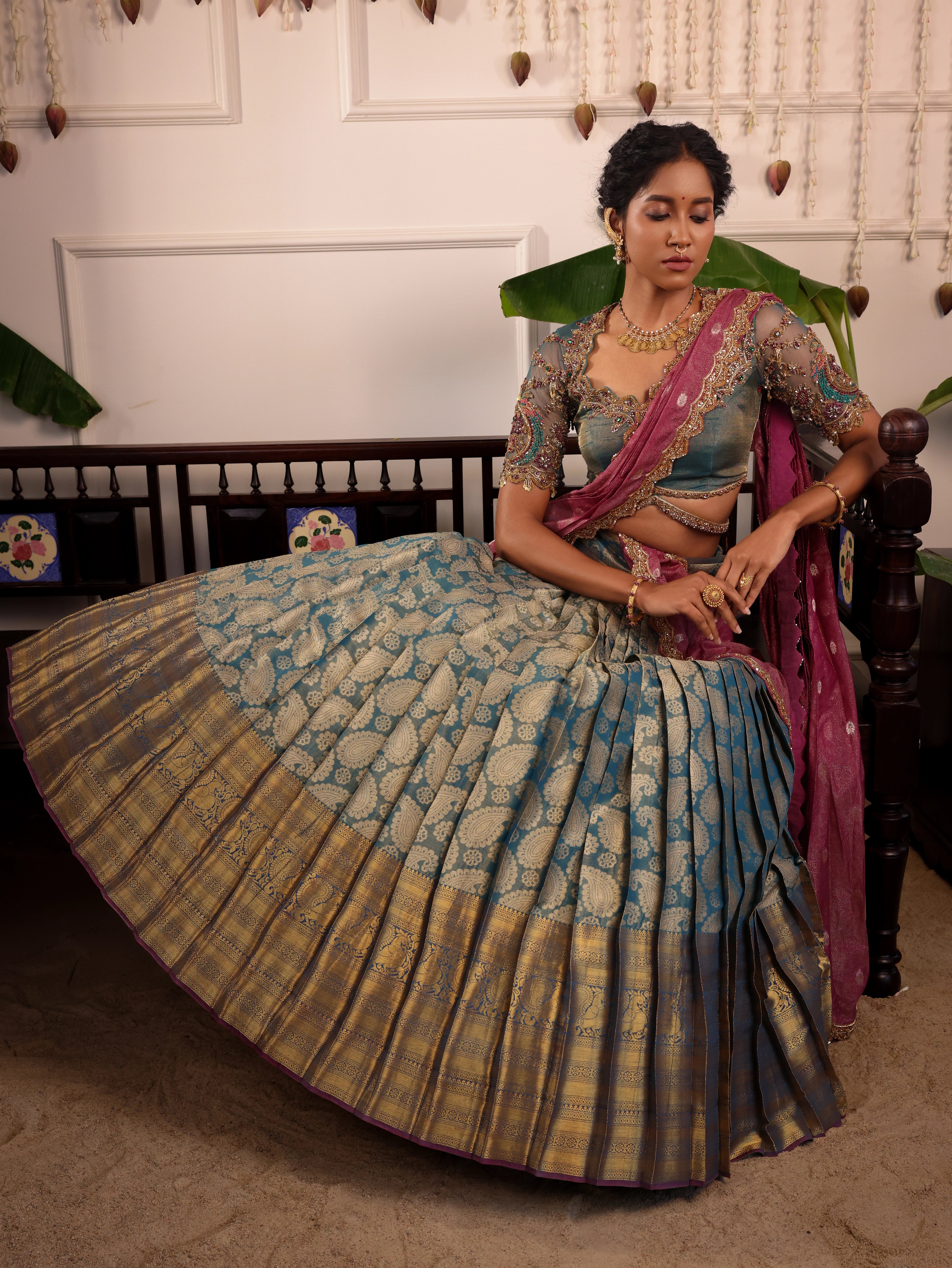 Model Gayathri Dhanasekar posing seated in a green silk half saree handcrafted by team Archana Karthick. Styled with jewelry sets from vummidi bangaru jewellers.