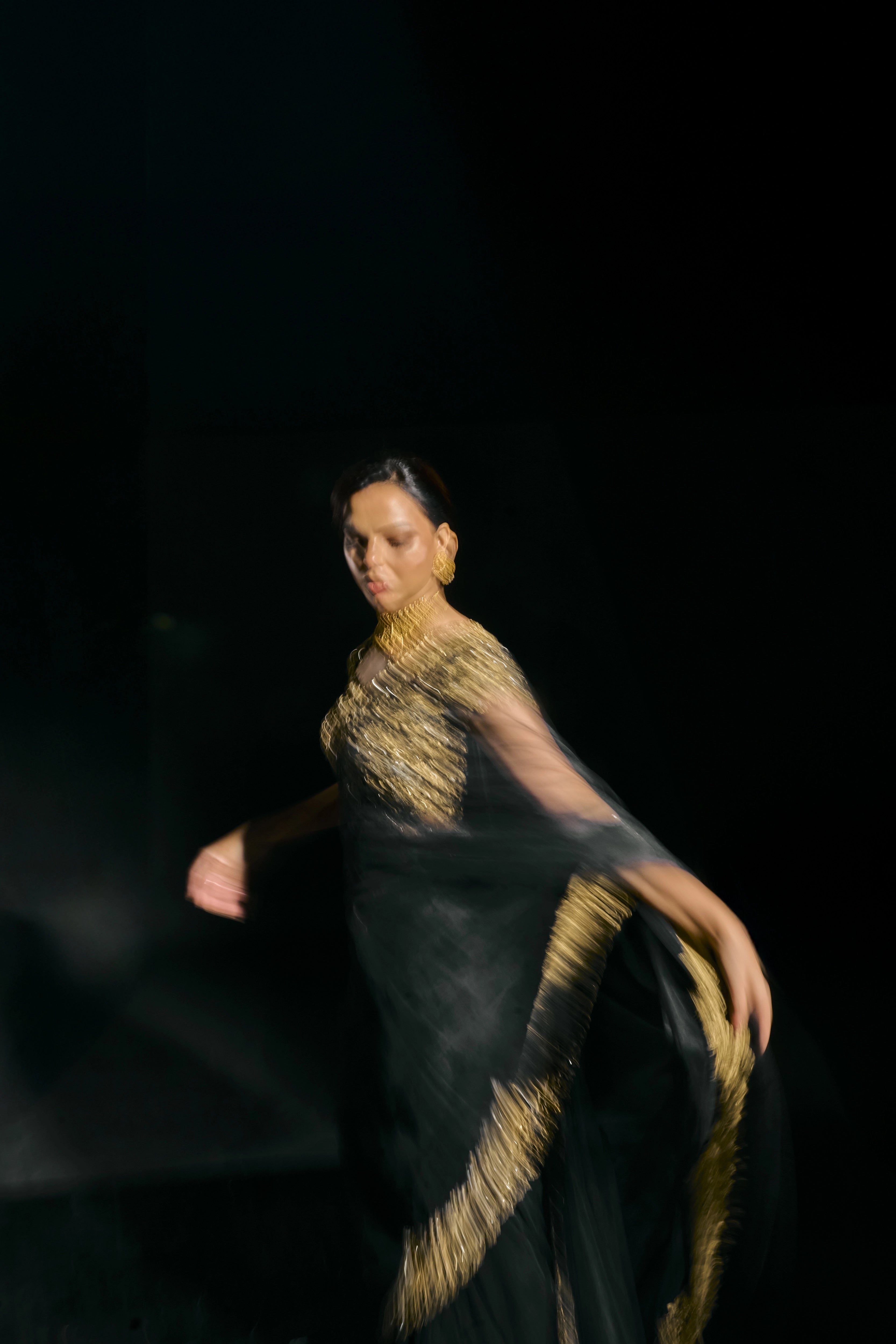 Model Jane C Thompson posing blurred in a black net saree with a gold blouse, handcrafted with zari, zardosi, sequins, stones and crystals for "HAZE" - A/W'25 capsule collection by Archana Karthick.