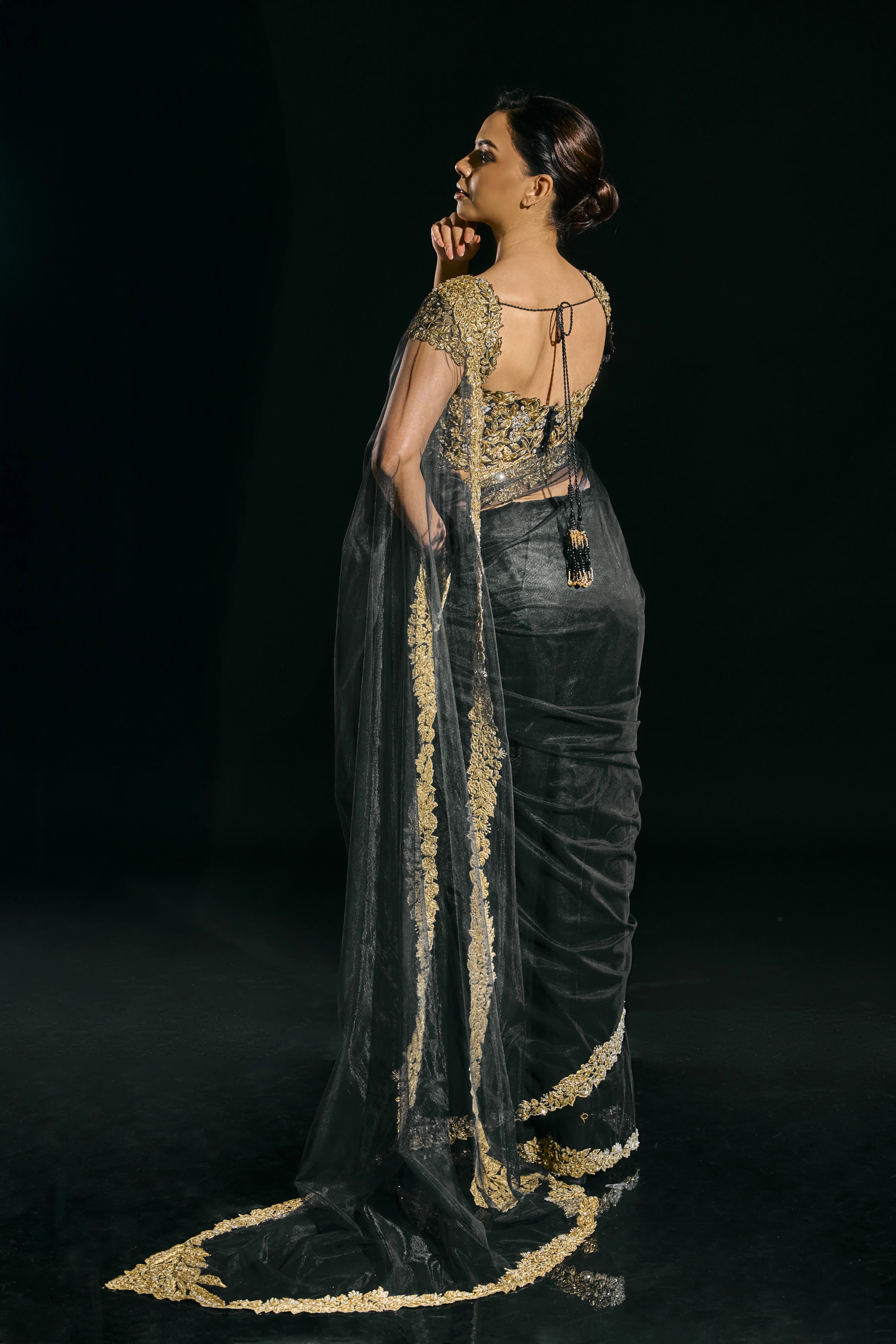Model Jane C Thompson posing for a photoshoot in a black net saree with a gold blouse and showcasing back design, handcrafted with zari, zardosi, sequins, stones and crystals for "HAZE" - A/W'25 capsule collection by Archana Karthick.