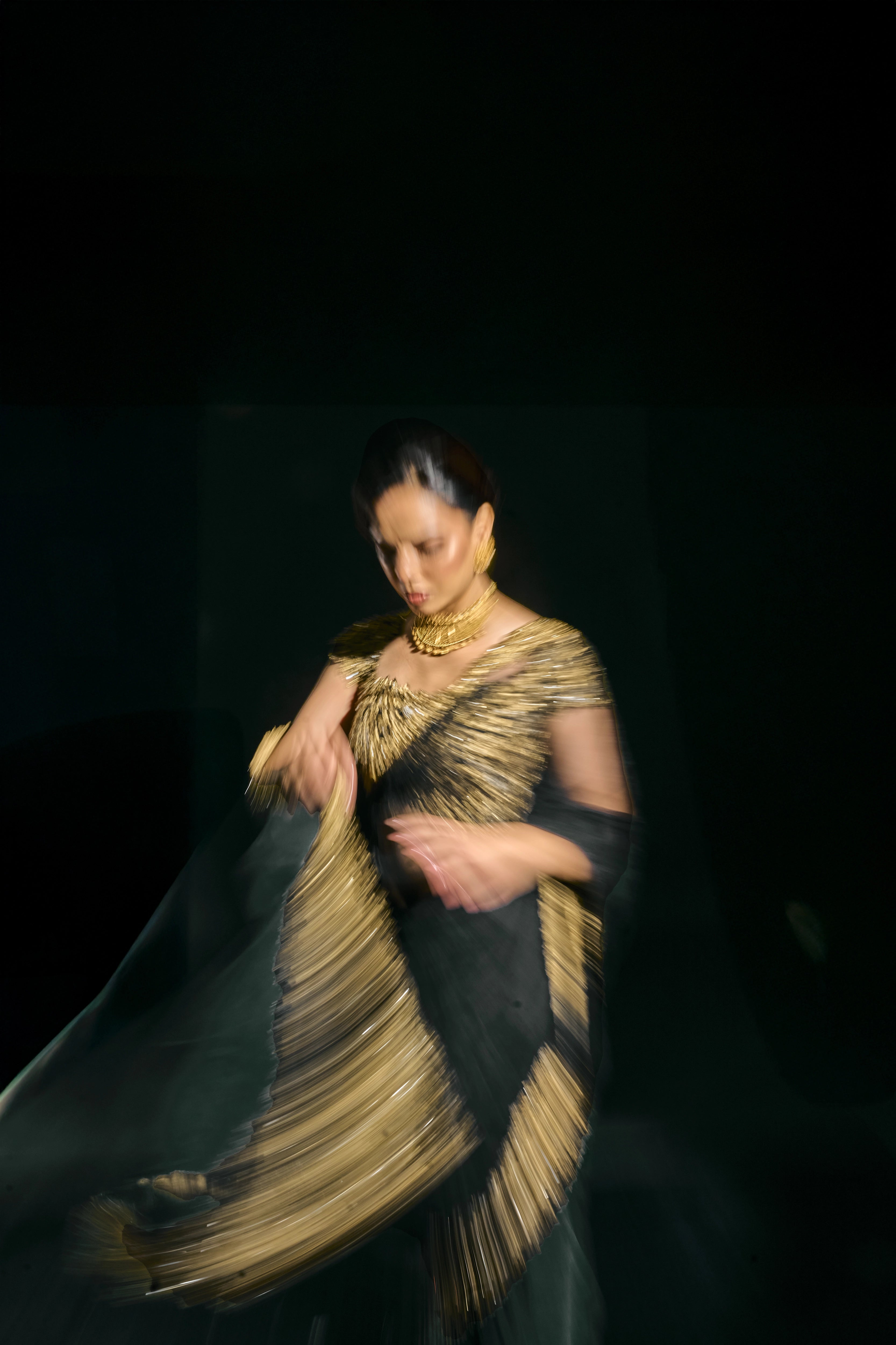 Model Jane C Thompson posing for a photoshoot in a black net saree with a gold blouse, handcrafted with zari, zardosi, sequins, stones and crystals for "HAZE" - A/W'25 capsule collection by Archana Karthick.