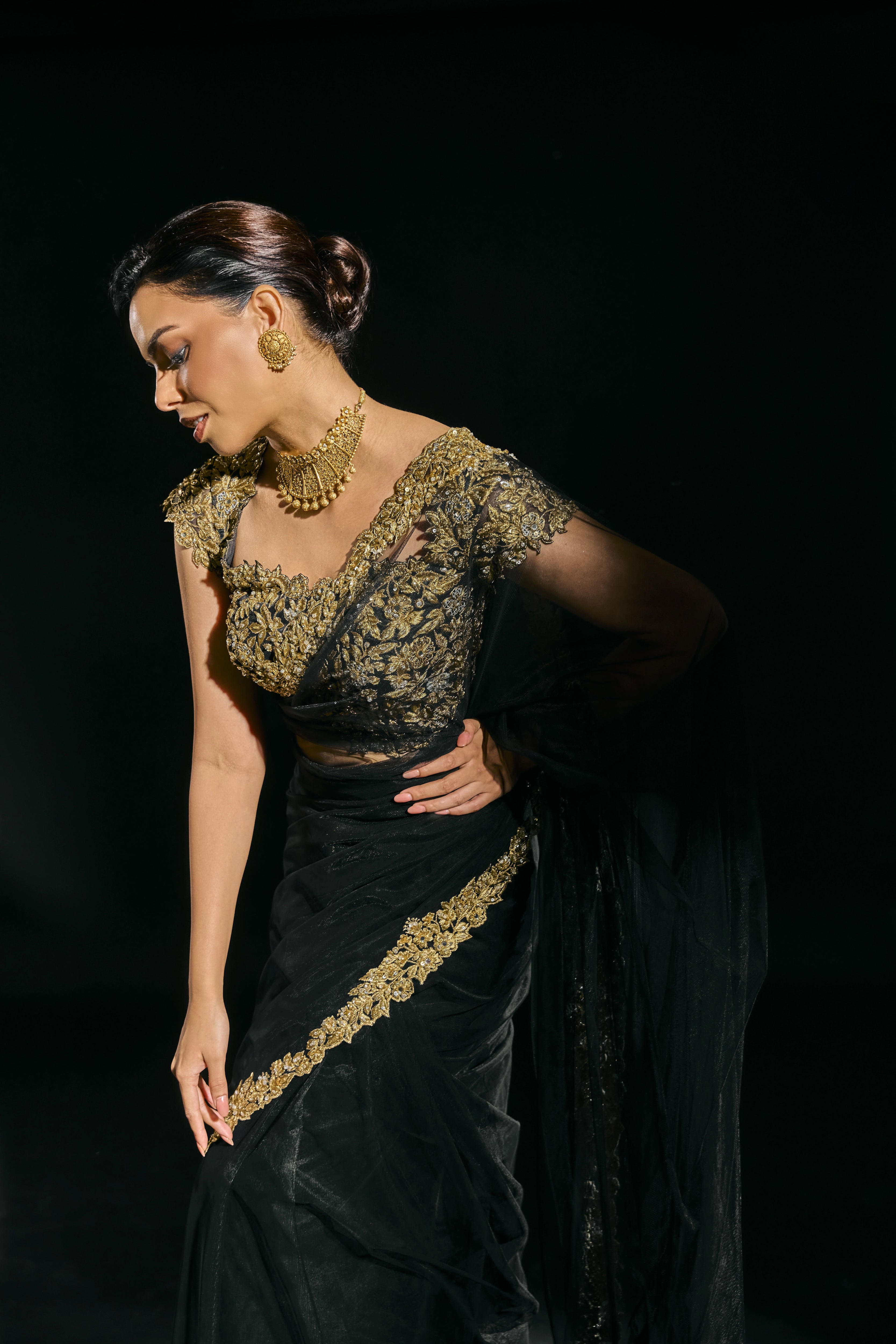 Model Jane C Thompson posing in a black net saree with a gold blouse, handcrafted with zari, zardosi, sequins, stones and crystals for "HAZE" - A/W'25 capsule collection by Archana Karthick.