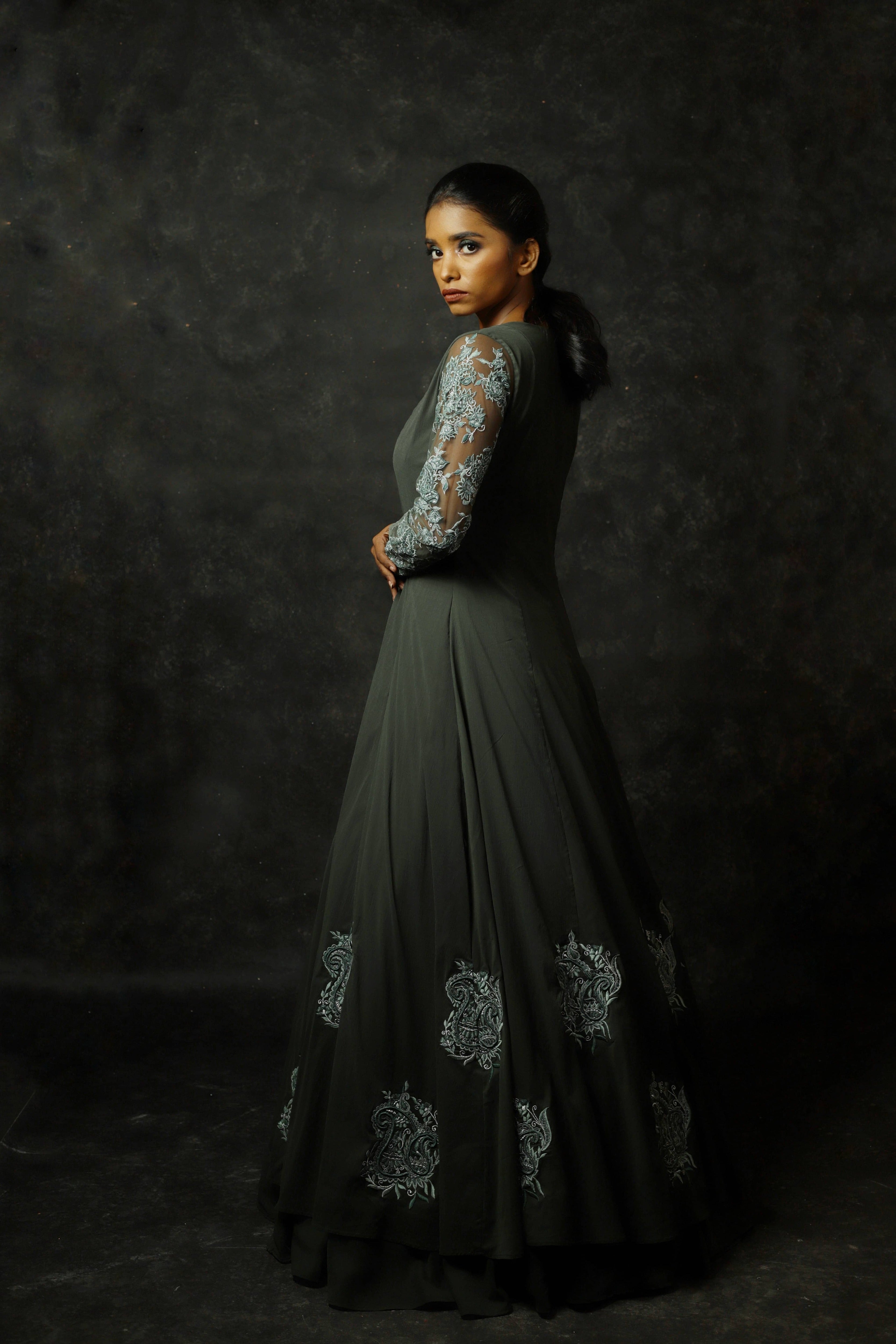 Model Posing looking over her back at the lens an olive green georgette masakali lehenga with long shrug and bralette.