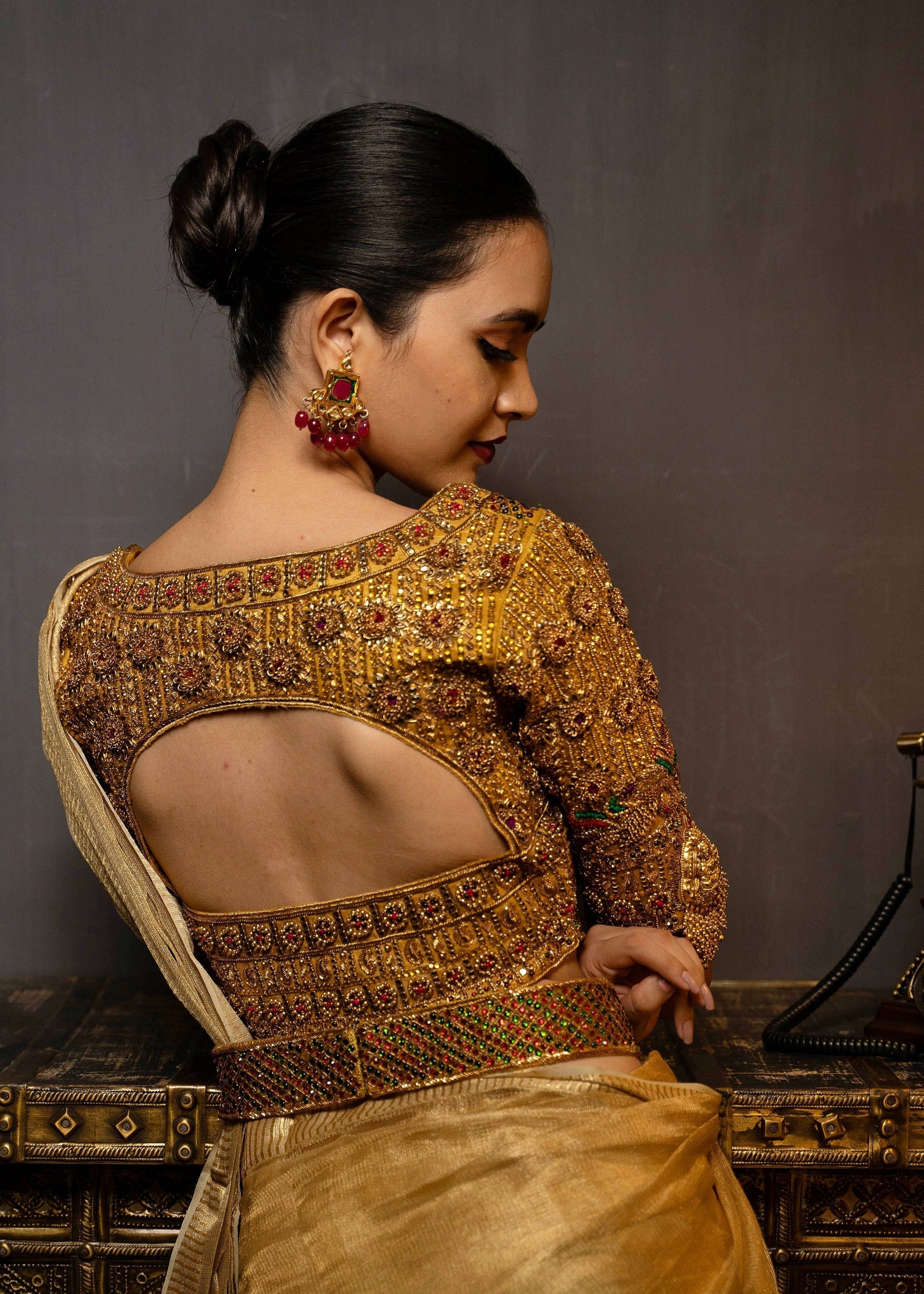 Model Preeti Kumari posing in a gold handcrafted raw silk blouse with heavy kemp embeliishment and goddess pendants on sleeves and matching belt. Blouse back design.