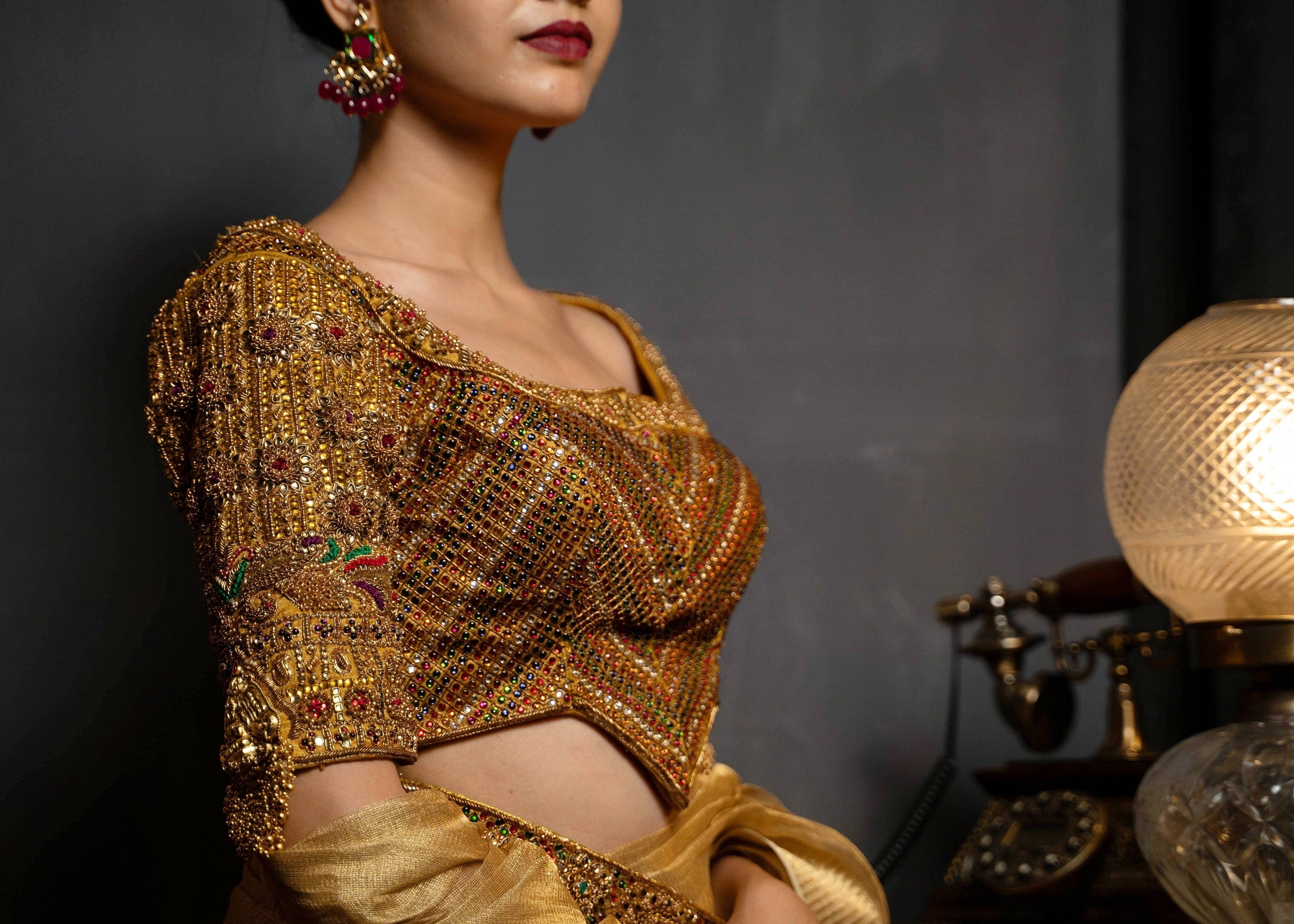 Model Preeti Kumari posing in a gold handcrafted raw silk blouse with heavy kemp embeliishment and goddess pendants on sleeves and matching belt. Blouse front and work on cups.