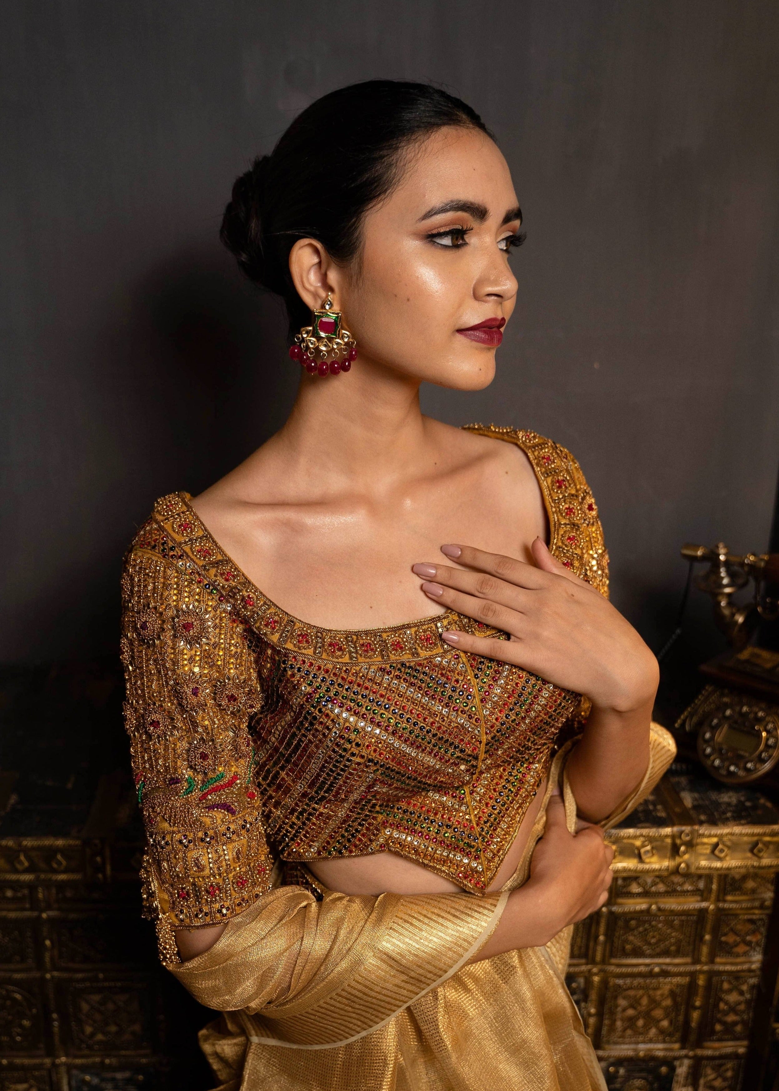 Model Preeti Kumari posing in a gold handcrafted raw silk blouse with heavy kemp embeliishment and goddess pendants on sleeves and matching belt. Blouse front and work on cups and neckline.